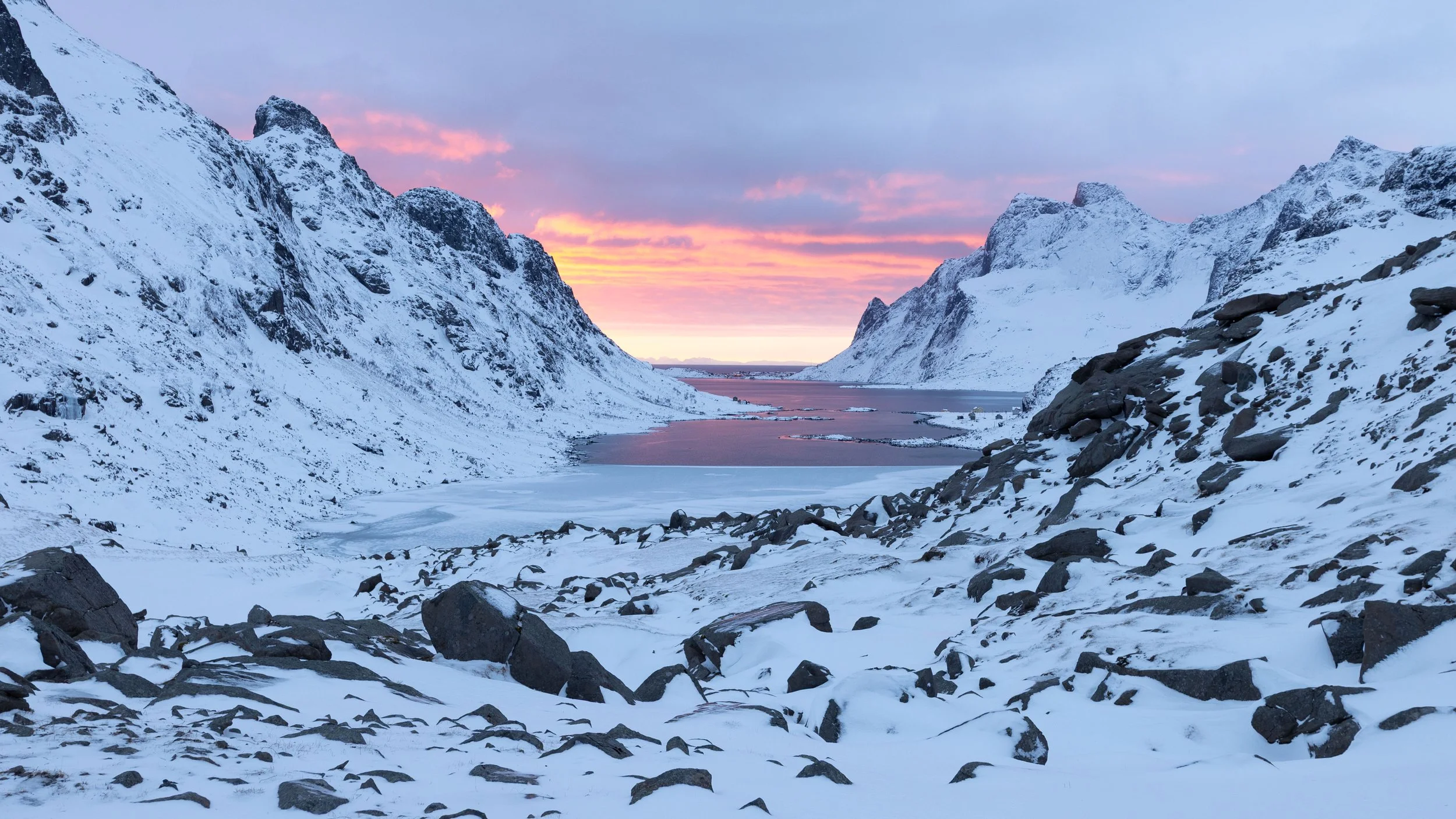Paisaje invernal de Lofoten con montañas cubiertas de nieve, fiordo al fondo y una suave luz rosada iluminando el cielo durante el amanecer en Vindstad, Lofoten