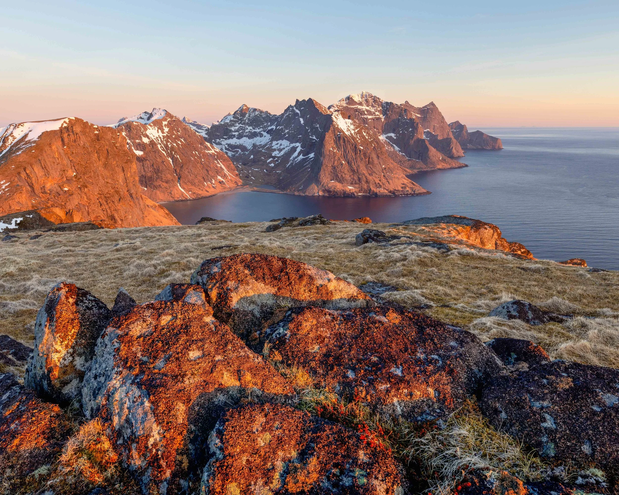 Vista de las montañas de Lofoten al atardecer, con luz dorada sobre las rocas, costa salvaje y el mar del norte de Noruega al fondo.