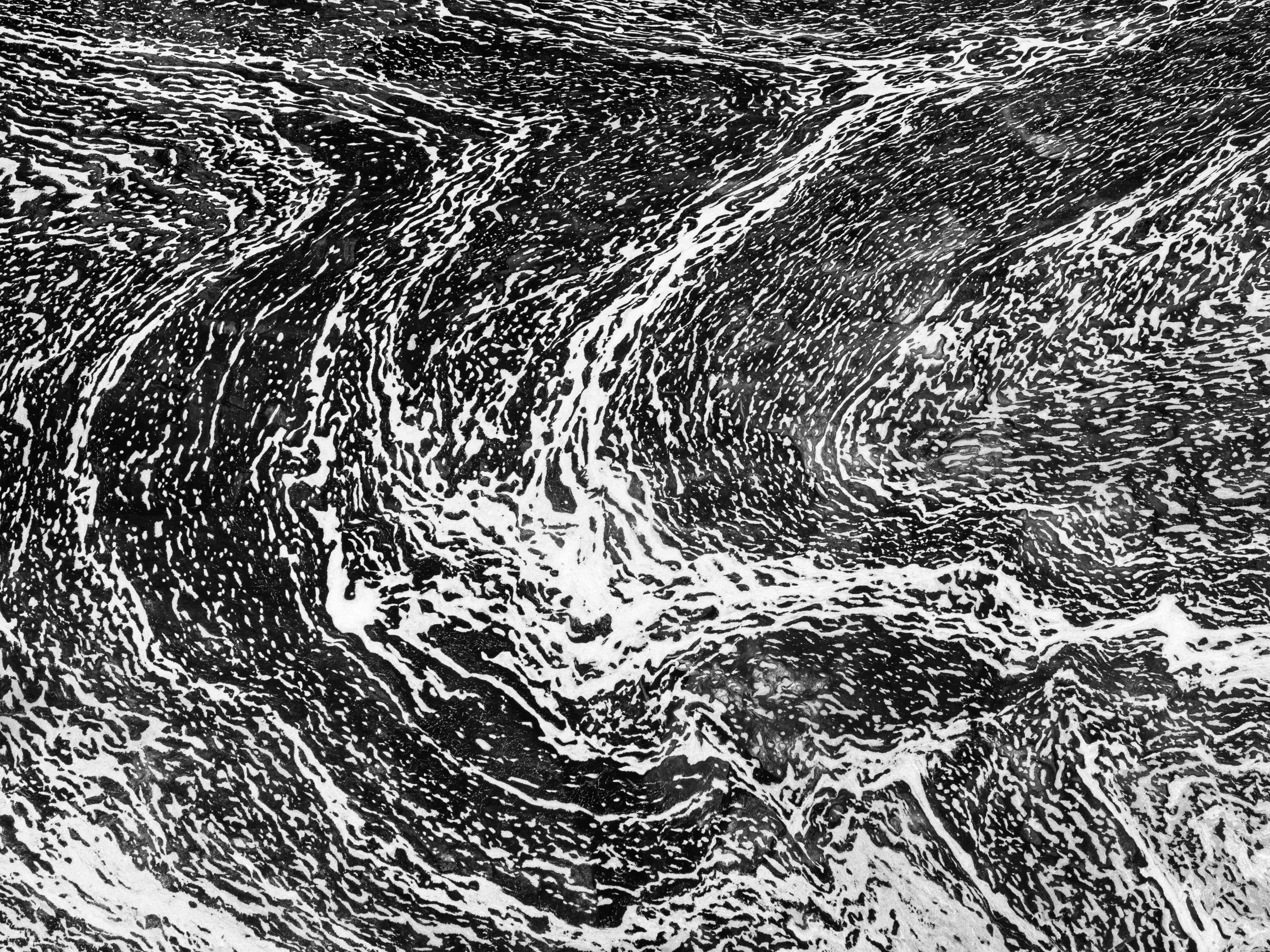 Fotografía abstracta de espuma en blanco y negro, con líneas orgánicas, contraste fuerte y patrones naturales sobre el agua.
