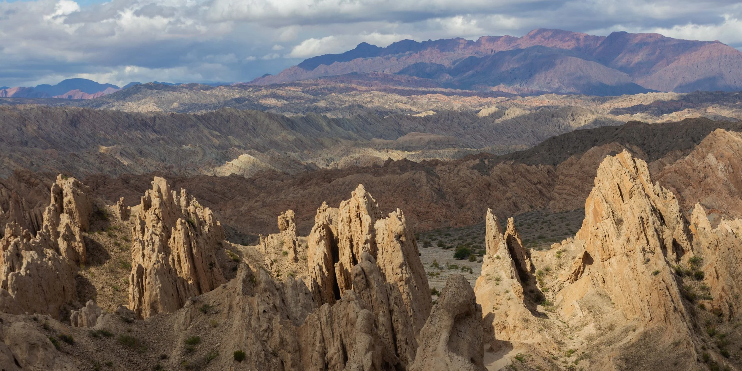 Quebrada de las Flechas en el norte argentino con formaciones rocosas erosionadas, montañas en capas y luz natural sobre un terreno árido y dramático.