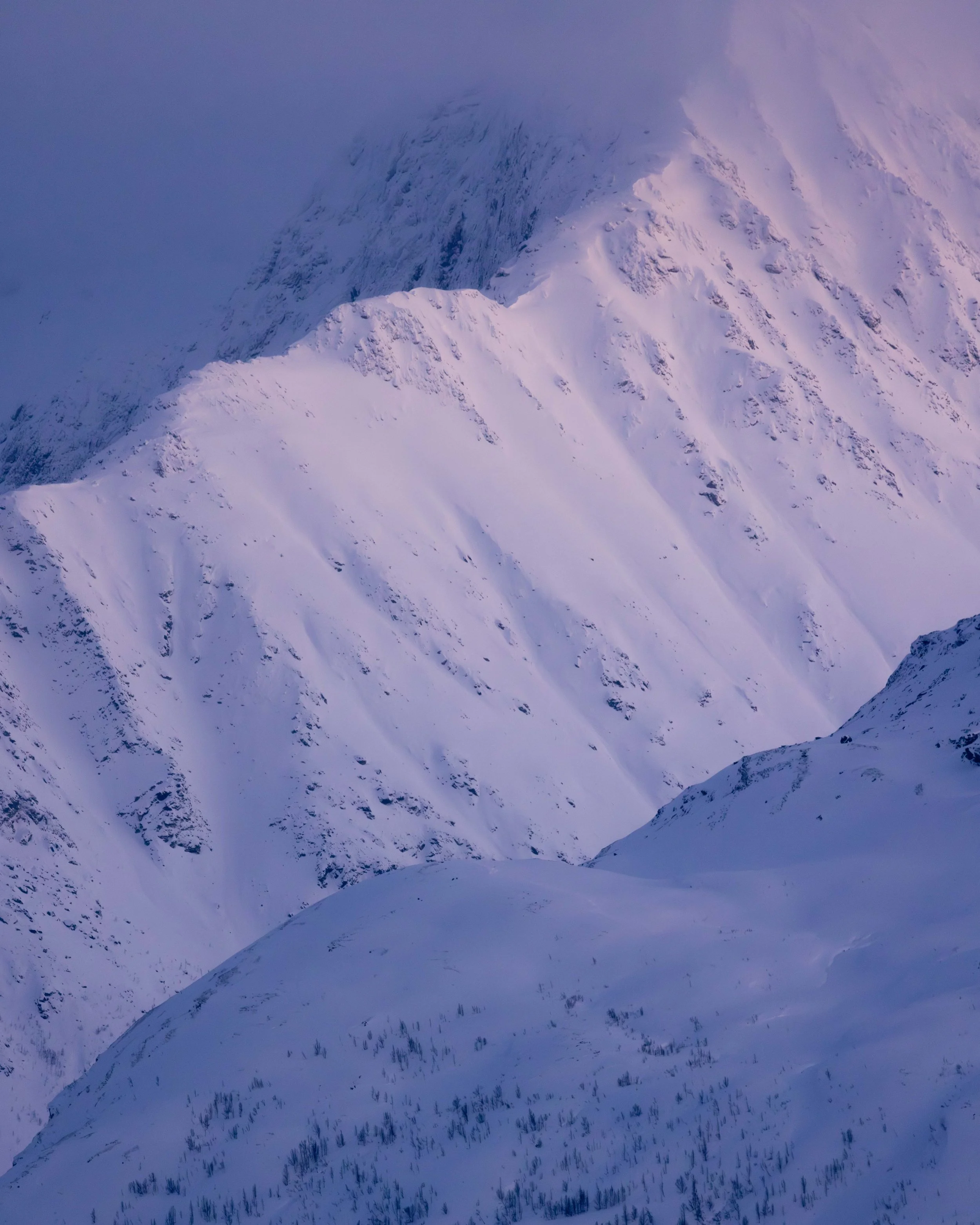 Fotografía de montaña nevada con tonos violetas y azules, capturando la textura de la nieve, las sombras suaves y la atmósfera fría del invierno.