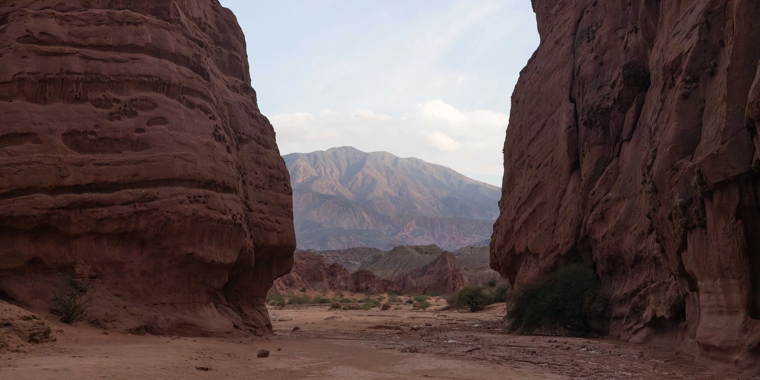 Paisaje árido del norte de Argentina, con un cañón de rocas rojizas que enmarca las montañas de fondo y revela la fuerza geológica, los colores terrosos y la belleza natural del paisaje andino.