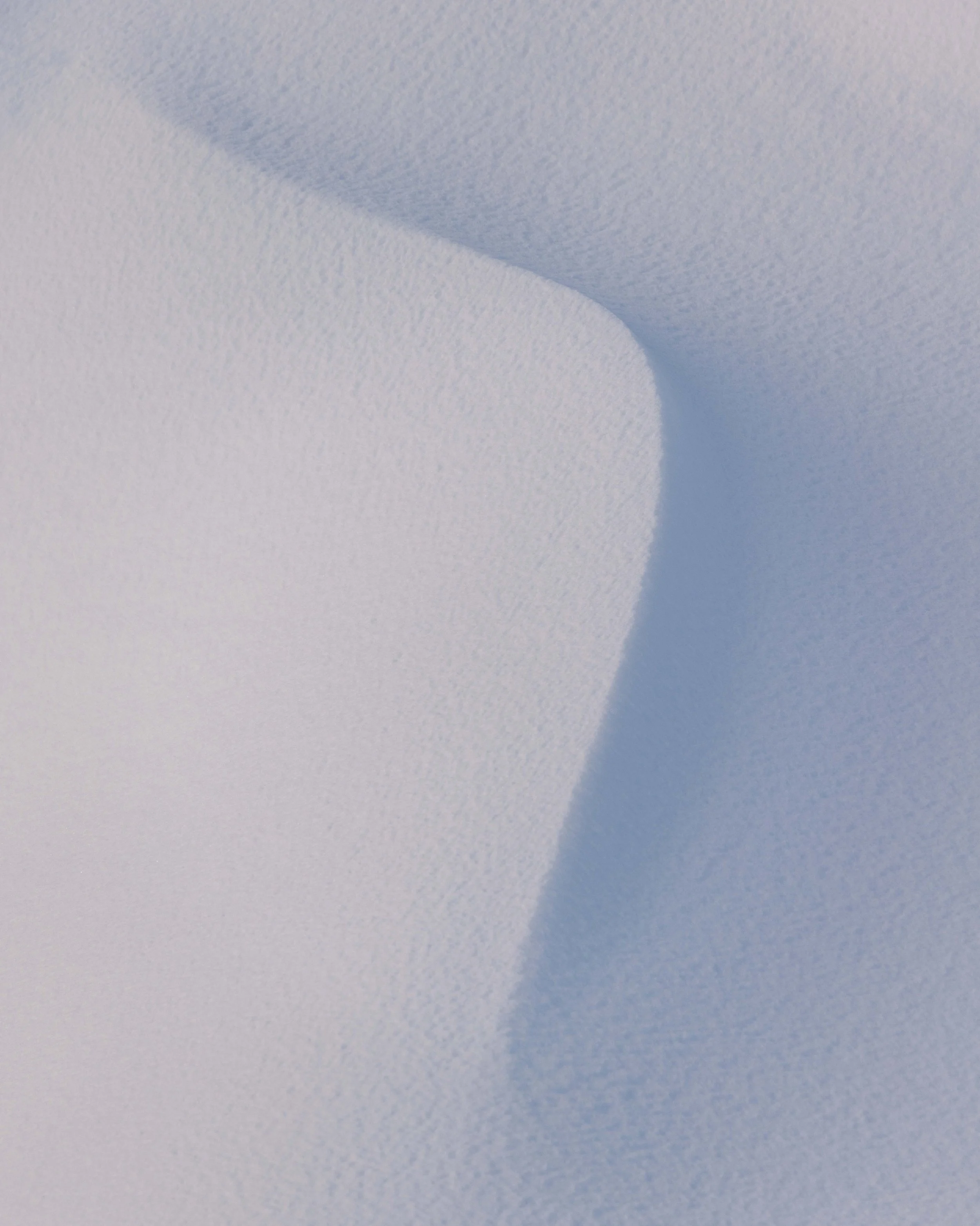 Fotografía minimalista de nieve con curvas naturales, sombras frías y una composición abstracta que resalta la suavidad del paisaje invernal.