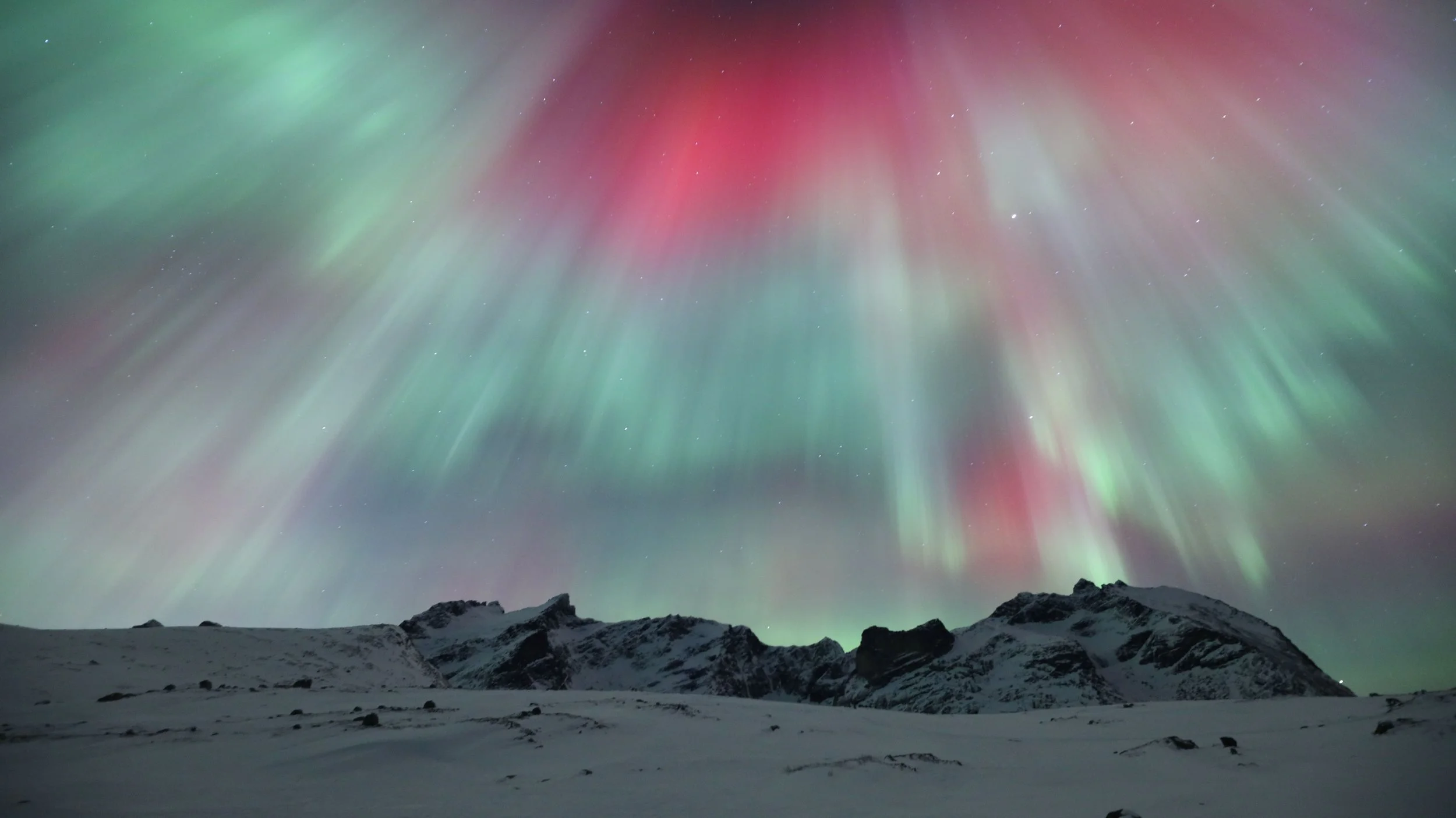Fotografía de aurora boreal con tonos rosados, rojos, azules, violetas y verdes sobre un paisaje nevado, capturando una noche de intensa actividad en el Ártico.