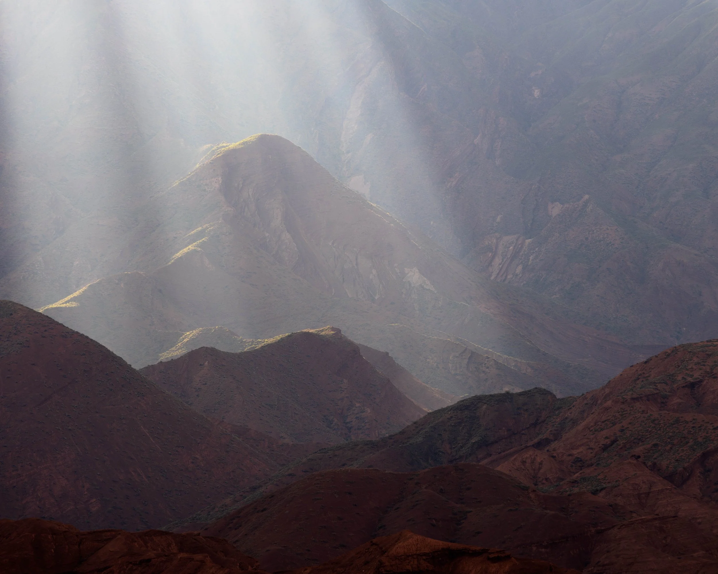 Fotografía atmosférica de montañas áridas con rayos de luz atravesando la neblina, creando profundidad, contraste y una sensación de inmensidad.