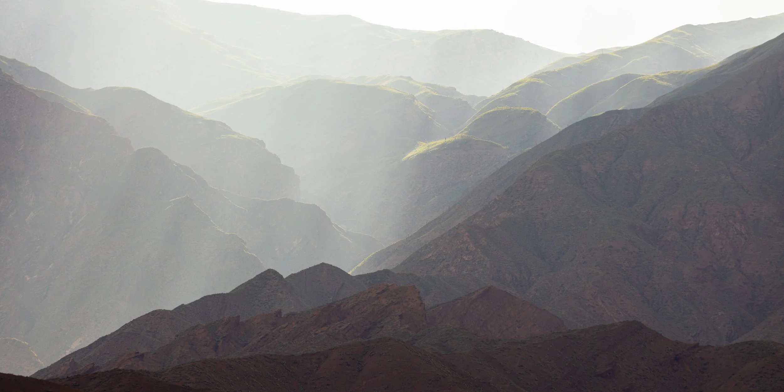 Paisaje de montañas áridas con capas superpuestas, luz suave y atmósfera brumosa, creando una imagen serena y profunda del relieve natural.