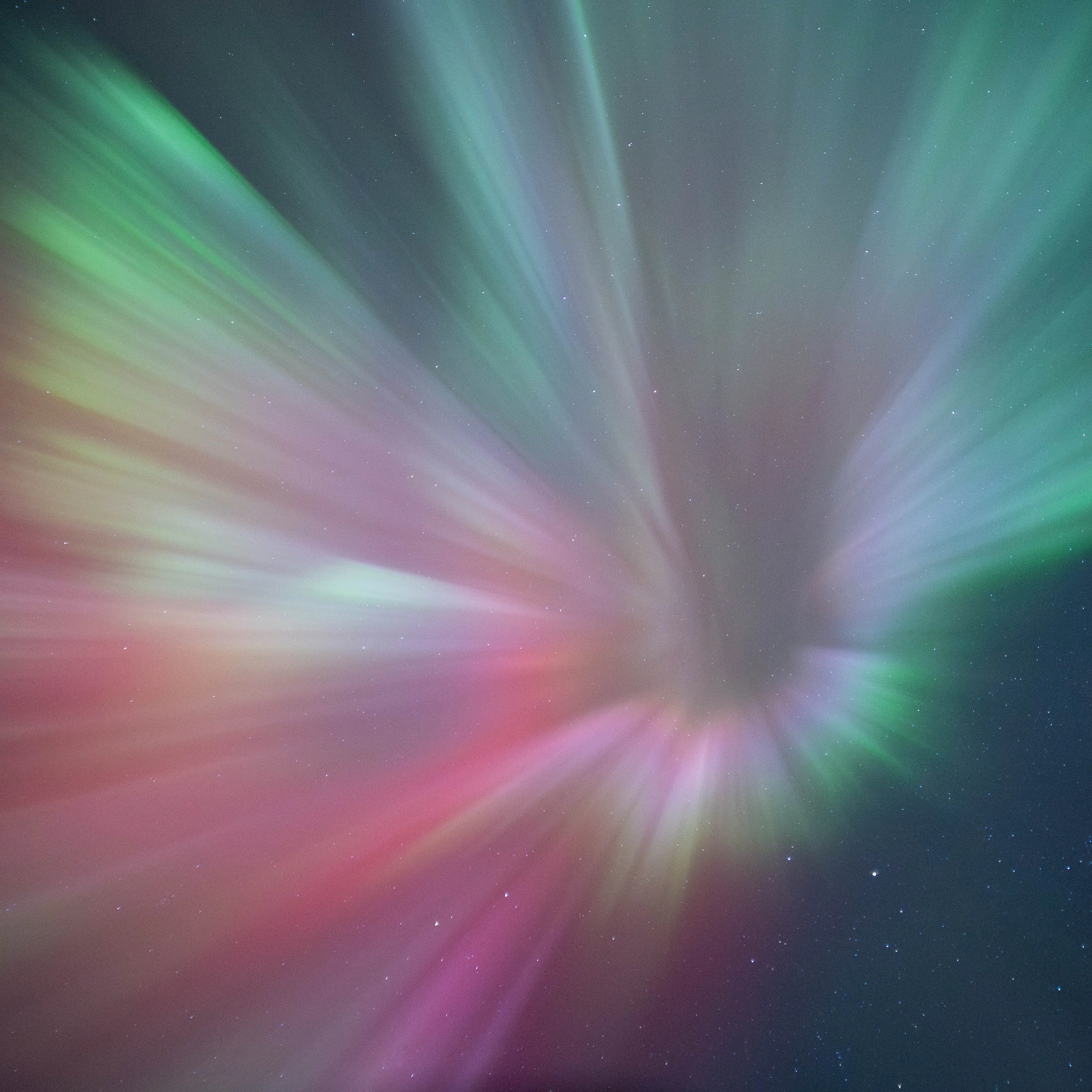 Imagen abstracta de aurora boreal con forma de flor durante una intensa actividad geomagnética, con luces verdes, rosadas, rojas, azules, amarillas, naranjas y violetas extendiéndose sobre un cielo estrellado.