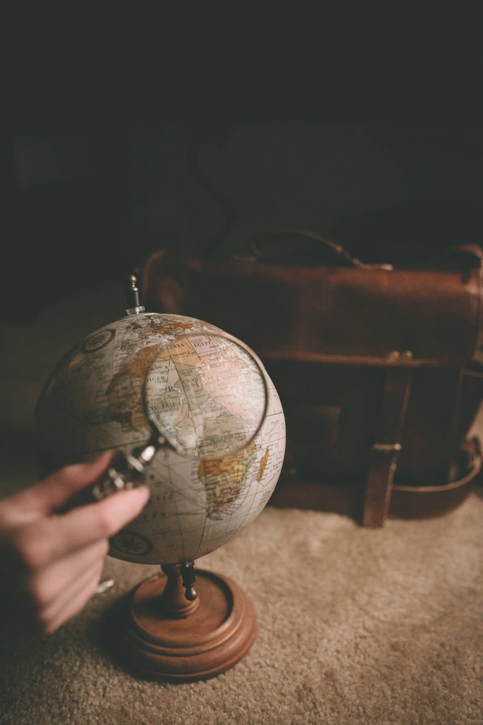 Hand holding a globe on a wooden stand, with a brown piece of furniture in the background.