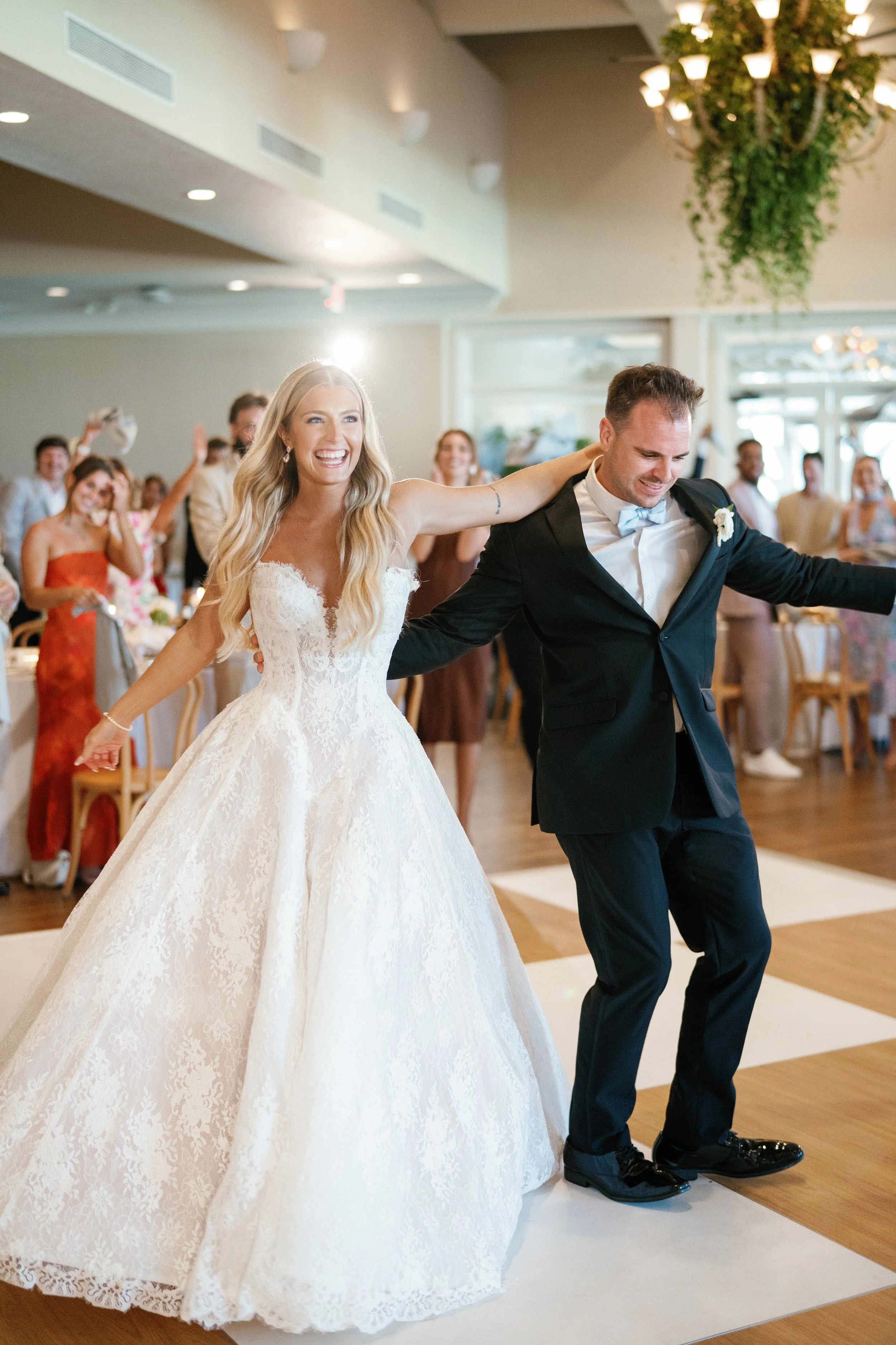 A bride and groom dancing at their wedding reception, with guests clapping and smiling in the background.