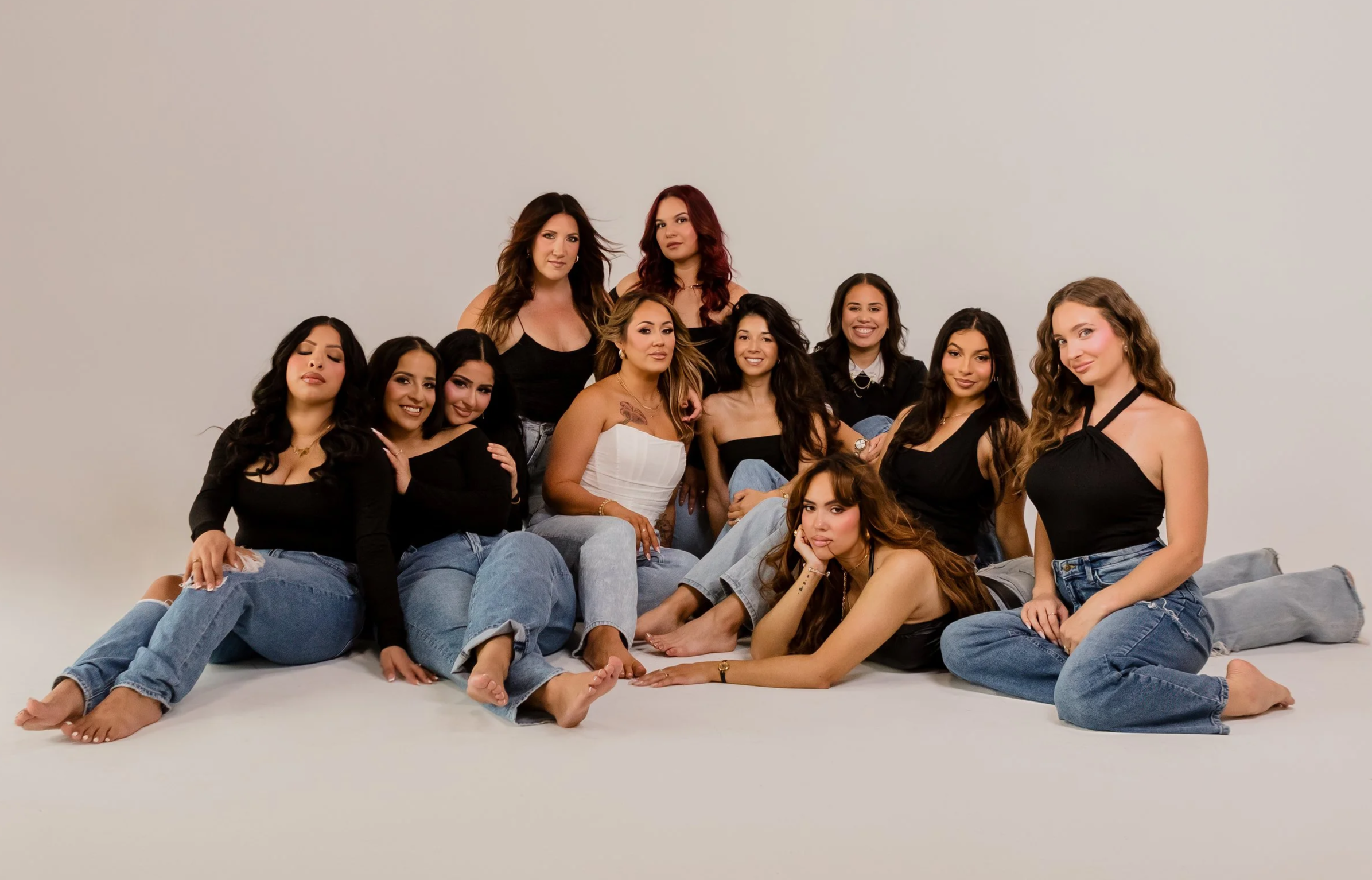 Group of hair and makeup artists posing together in casual outfits against a plain light-colored background.