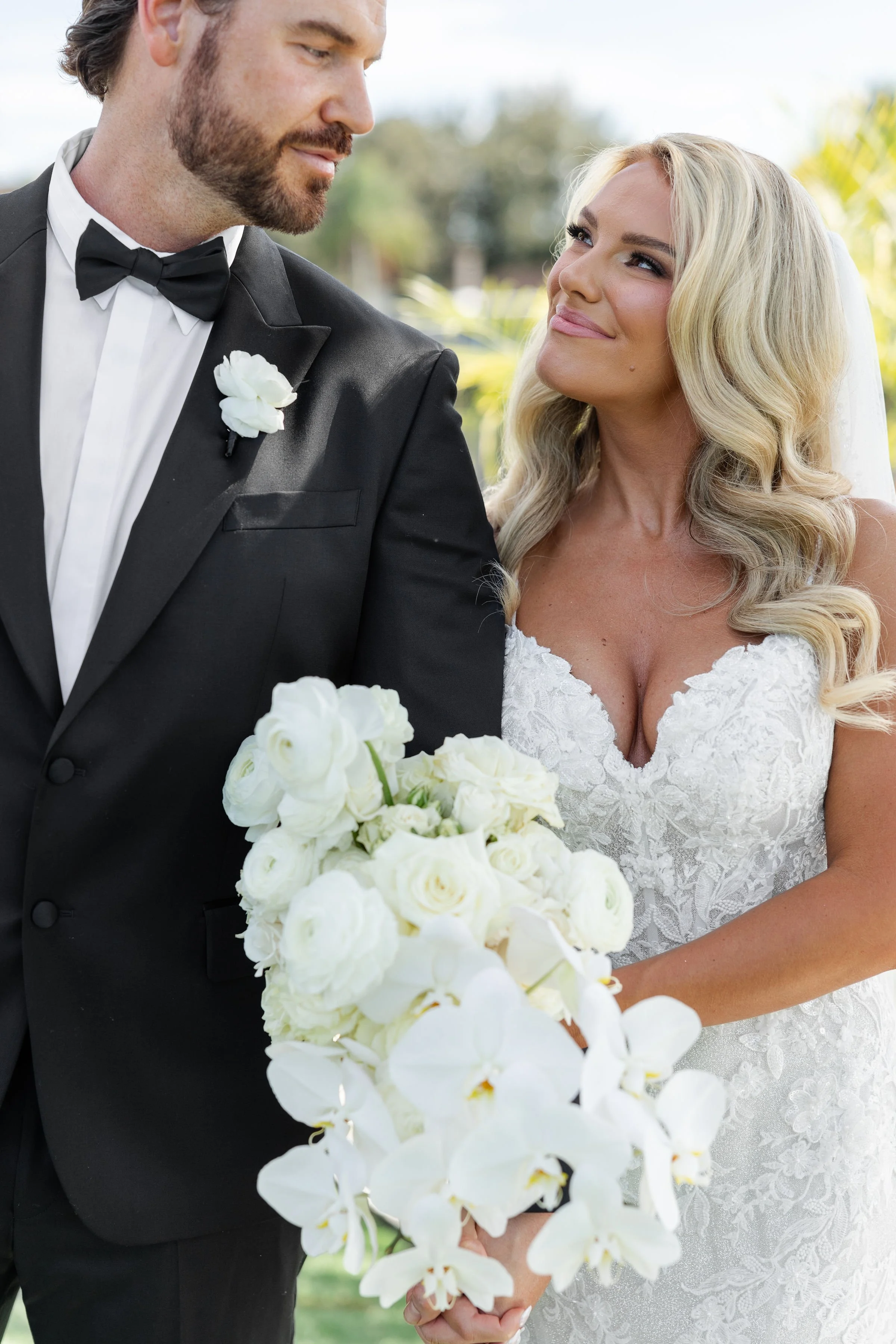 A bride and groom holding hands on their wedding day, with the bride holding a bouquet of white flowers.