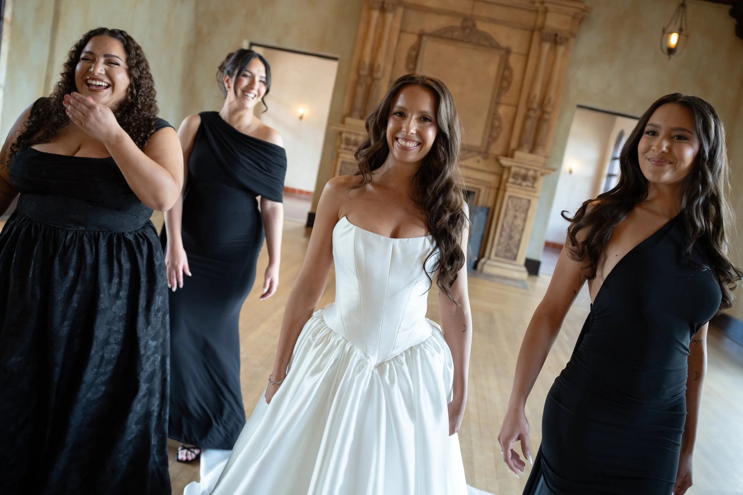 Four women in formal attire inside a decorated room, smiling and enjoying themselves.