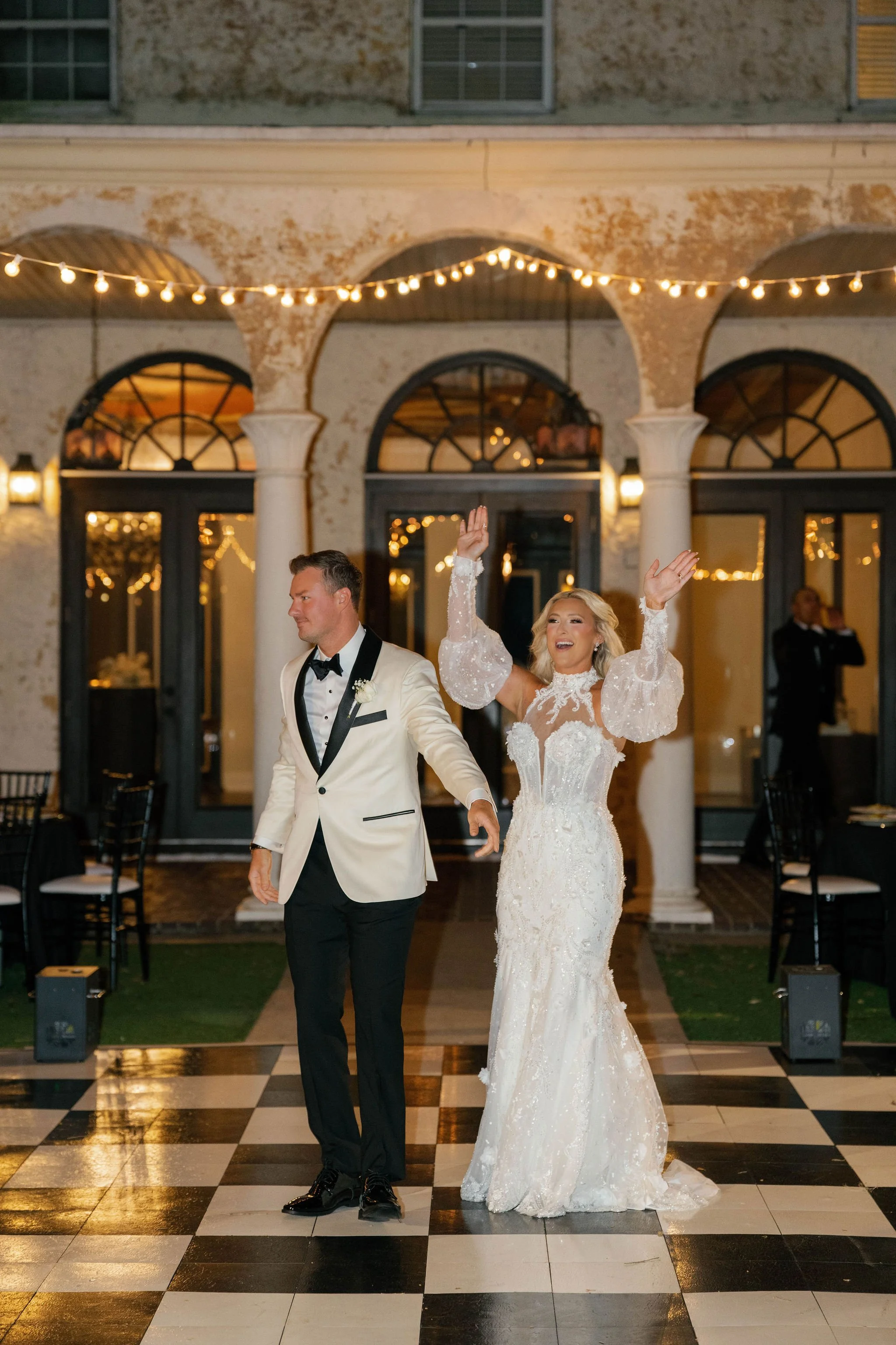 A bride and groom dancing at their wedding reception, with string lights overhead and an elegant venue background.