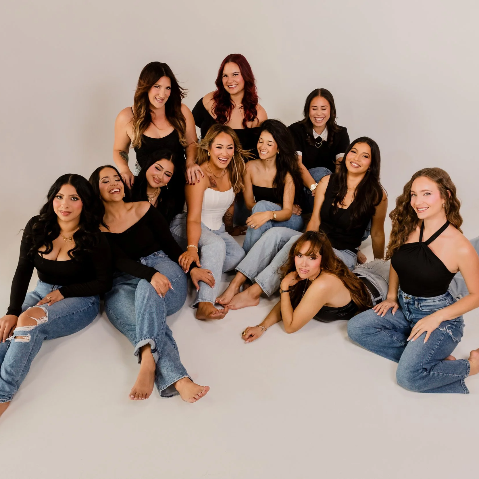Group of ten women in casual clothing posing together on a white background, smiling and laughing.