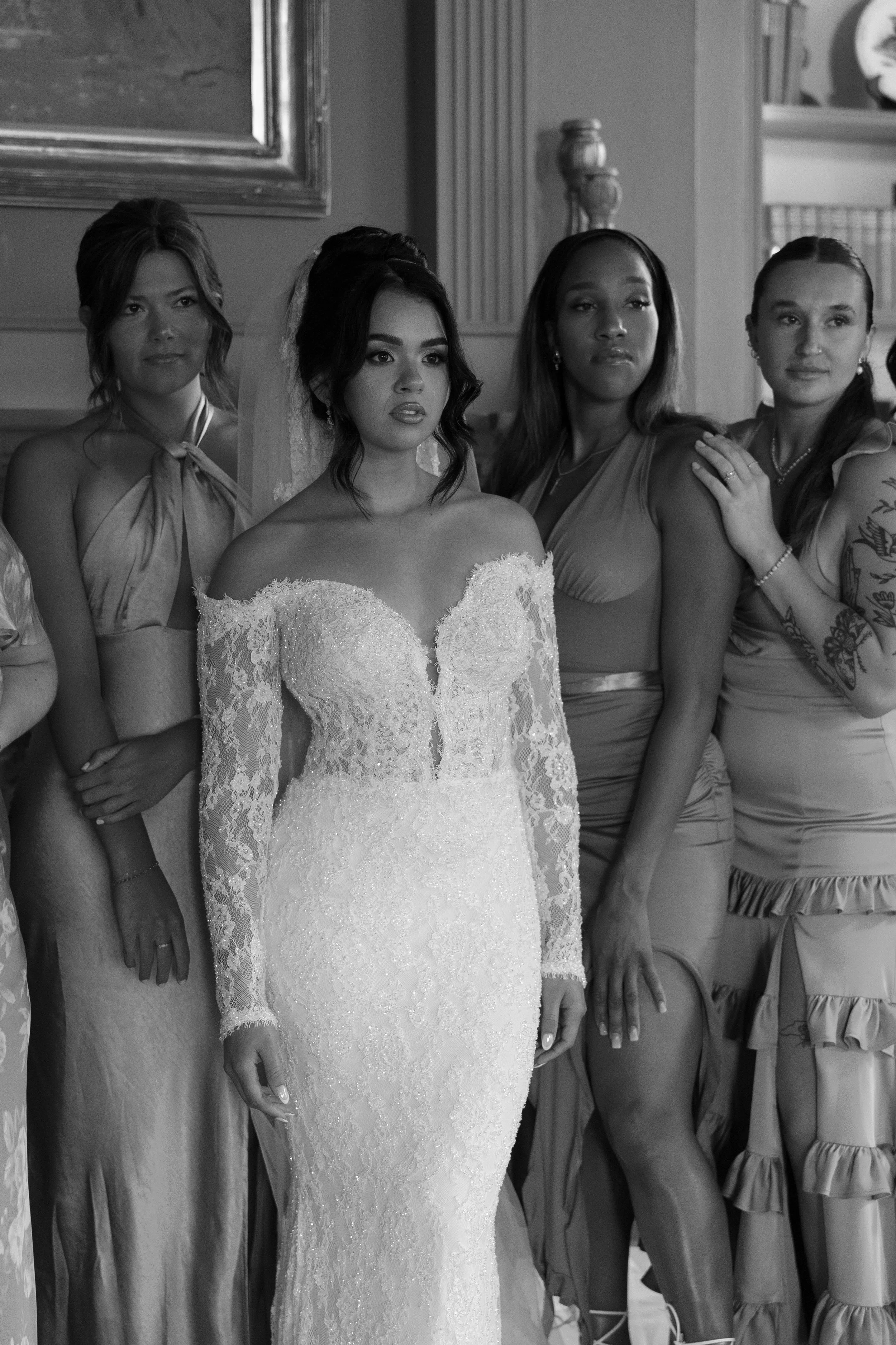 Group of women standing together indoors, with the central woman in a wedding gown, indicating a wedding celebration.