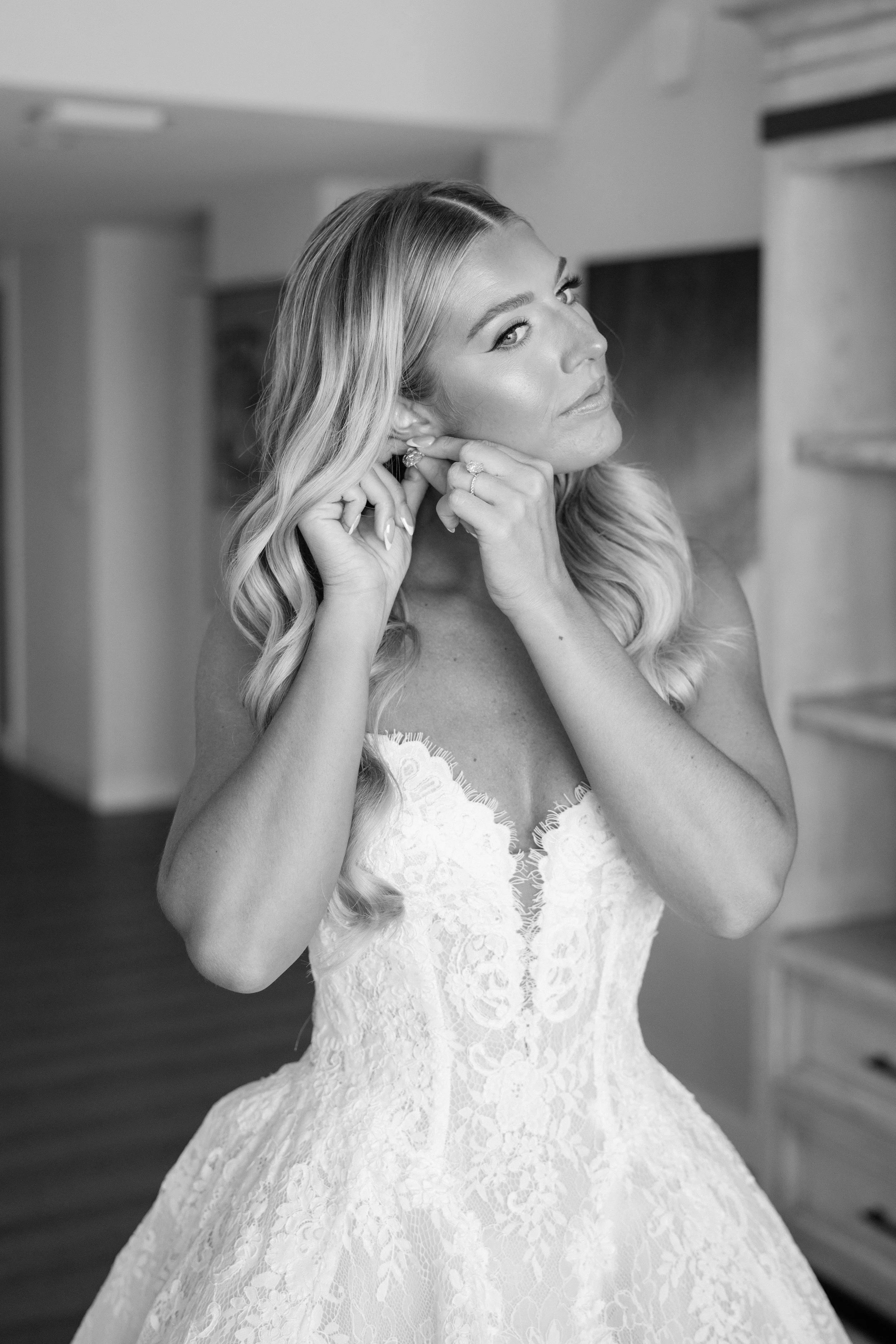 Black and white photo of a woman in a wedding dress putting on earrings.