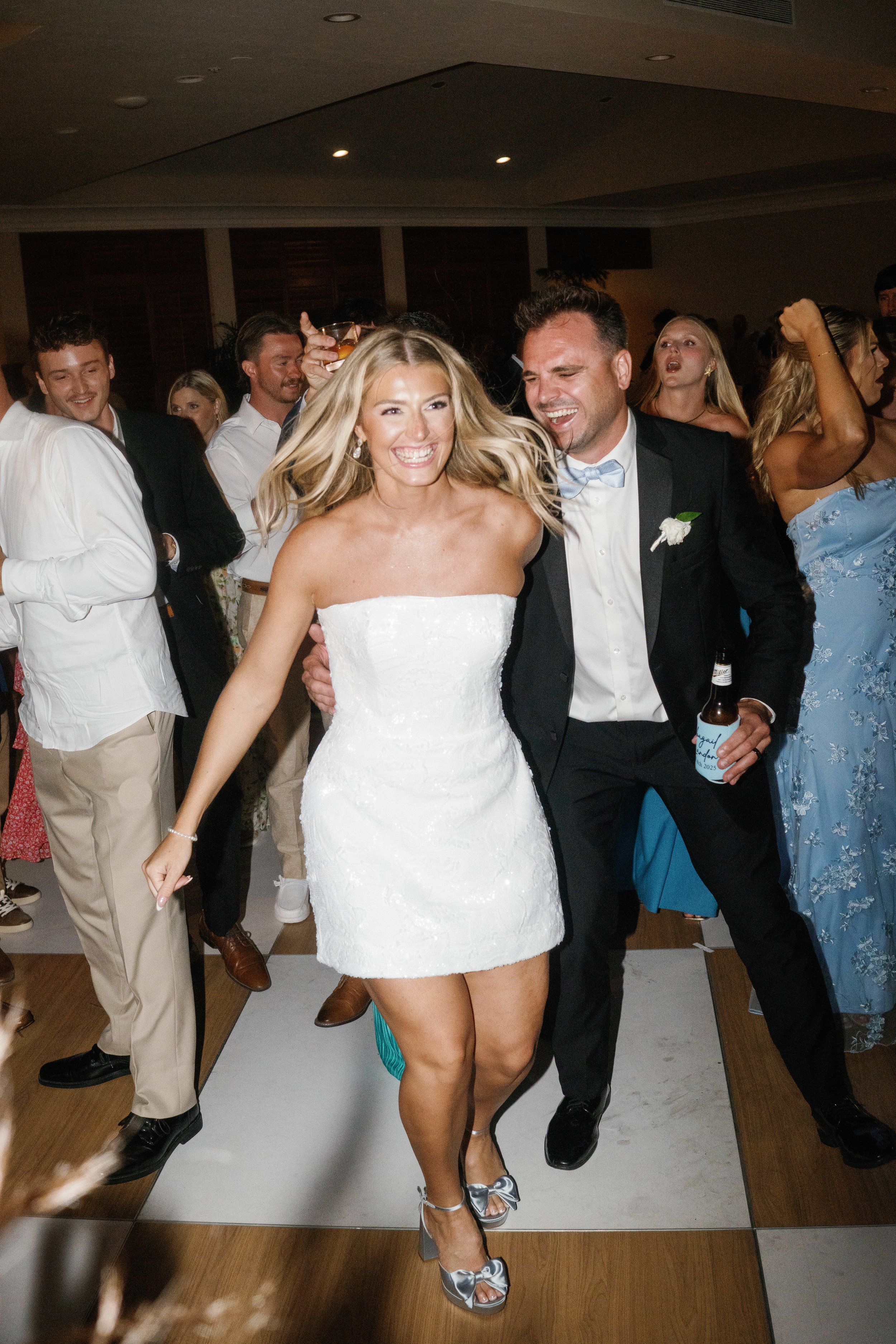 A bride and groom dancing and smiling at their wedding reception, surrounded by guests celebrating.
