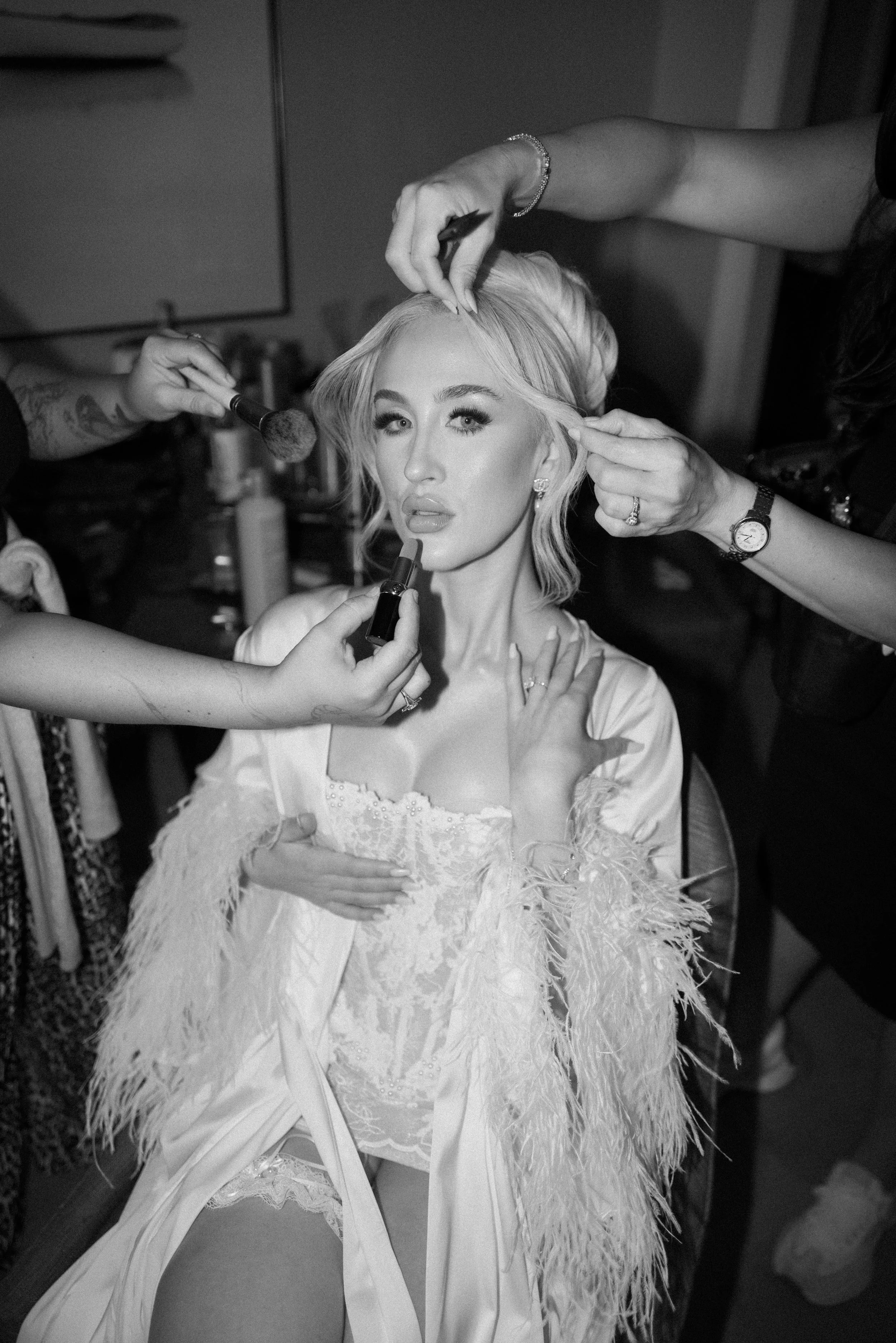 A woman in a wedding dress getting makeup done by multiple artists.
