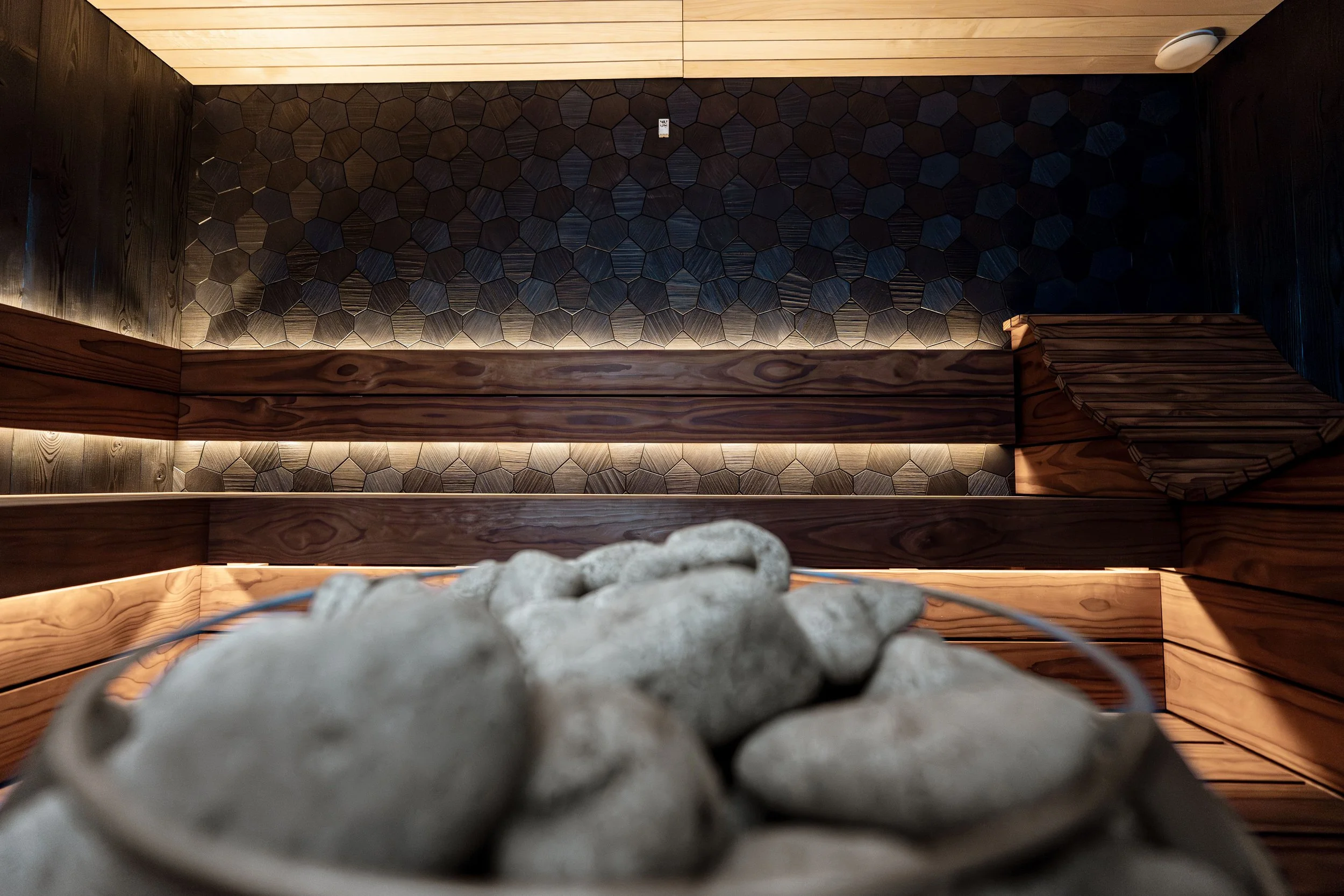 View of a decorated interior space with dark hexagonal tiles on the wall, wooden beams, and stone elements in the foreground.