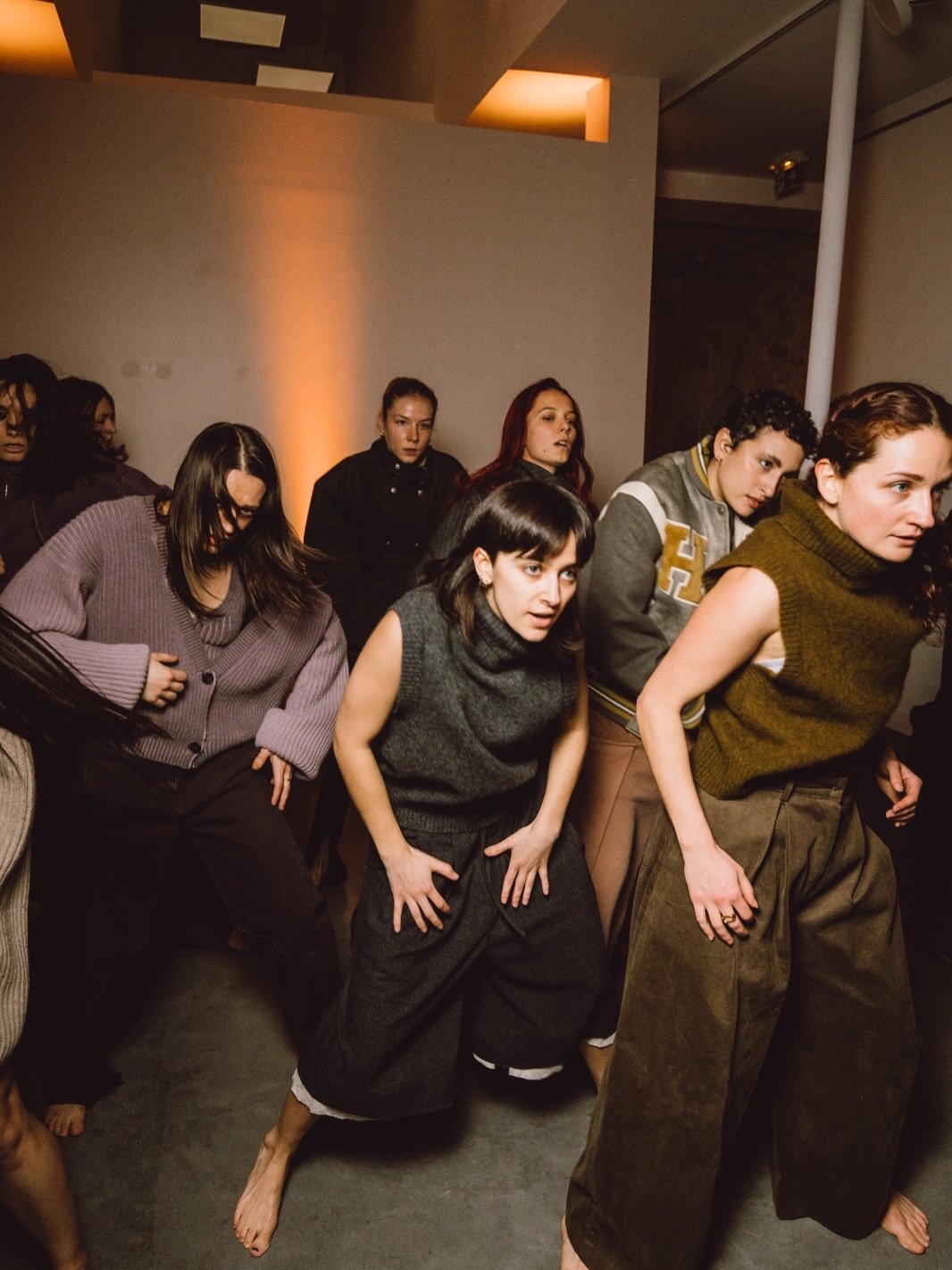 Group of women dancing at an indoor gathering, some with barefoot, in a room with warm lighting.