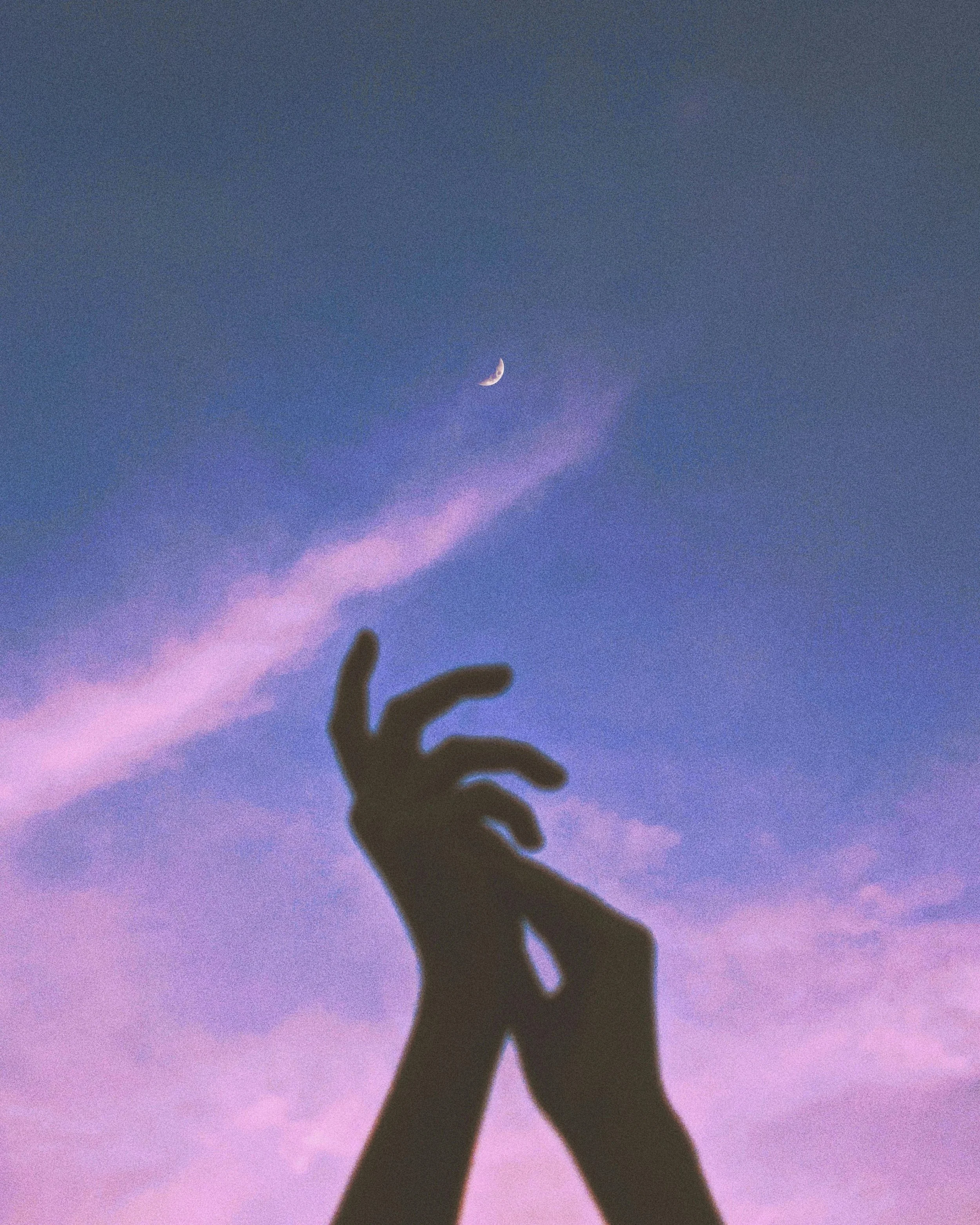 Silhouette of a person's hand and arm raised against a purple and blue sky with a crescent moon visible, with some blurred hand and thumb in the foreground.