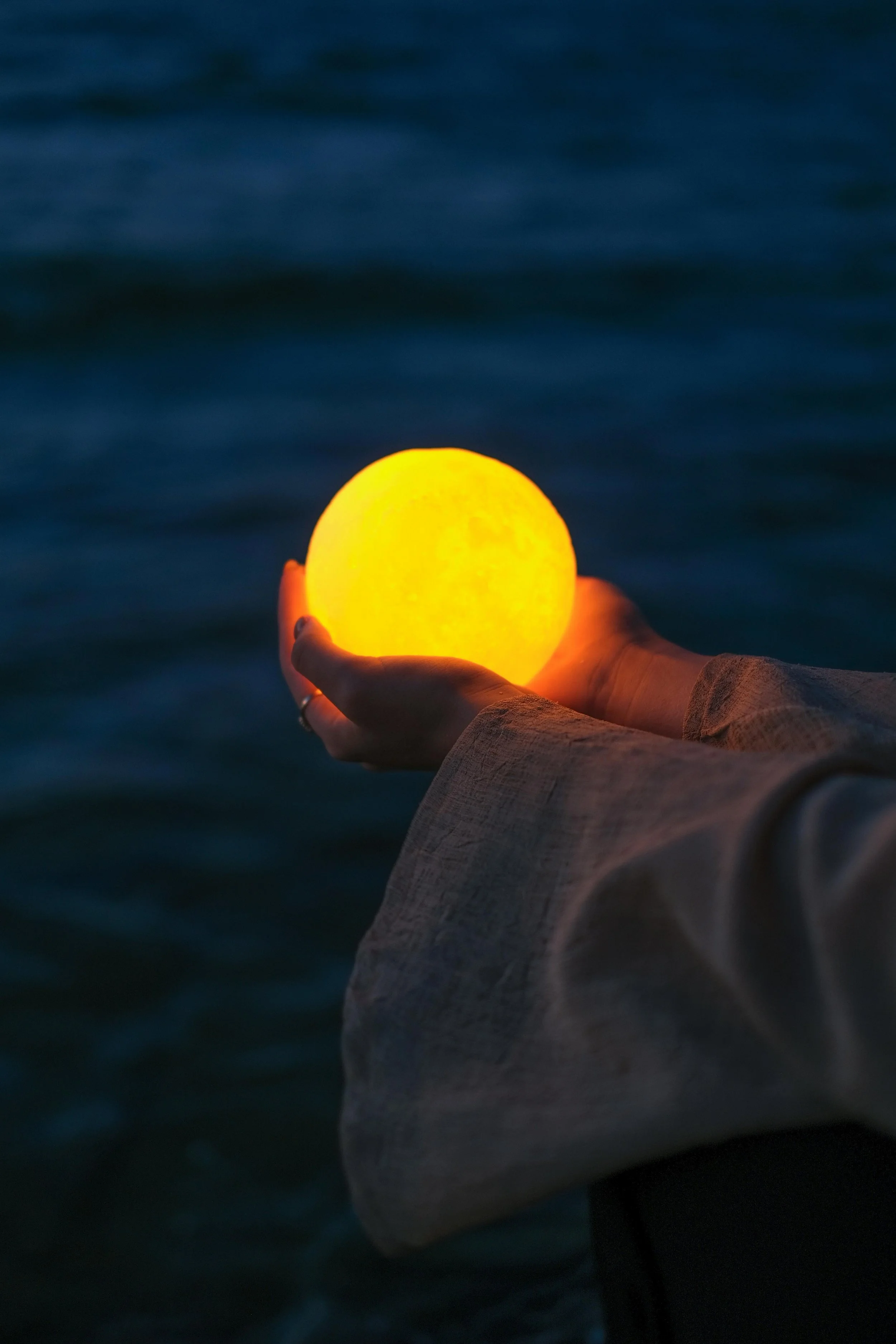 Person holding a glowing yellow orb against a dark blue water background.