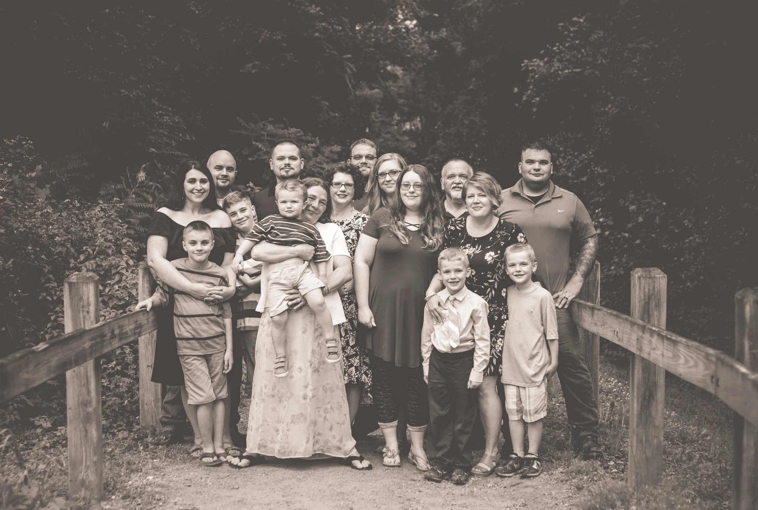 A large family group of adults and children standing outdoors on a wooded pathway, posing for a photo, in black and white.