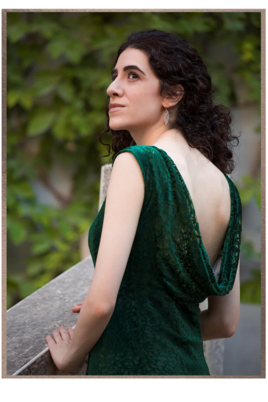 Portrait of Adi Denner in a green evening gown, looking over her shoulder beside a stone balustrade.
