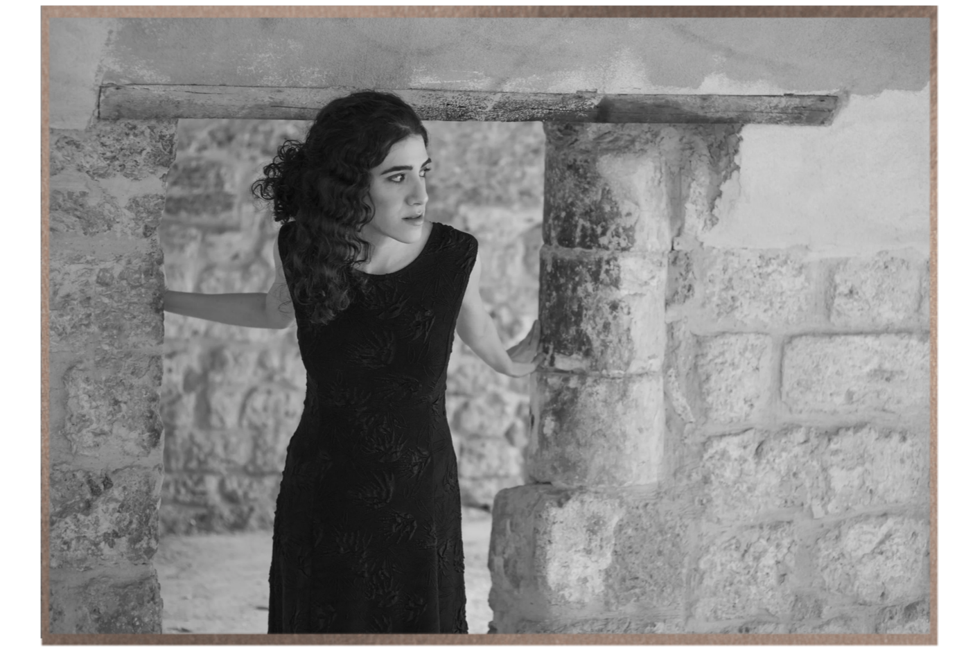 Black-and-white portrait of Adi Denner framed by an ancient stone doorway.