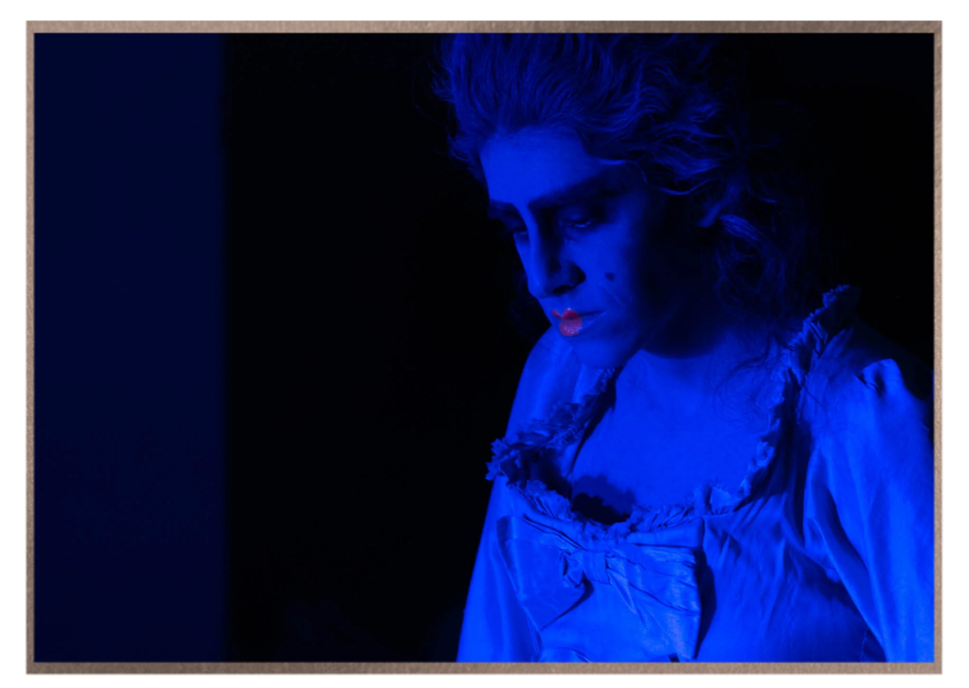 Adi Denner in character under striking blue stage lighting.