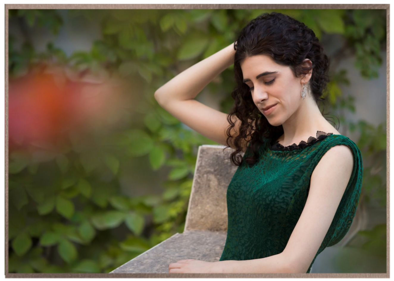 Portrait of Adi Denner in a green evening gown, standing among garden foliage.