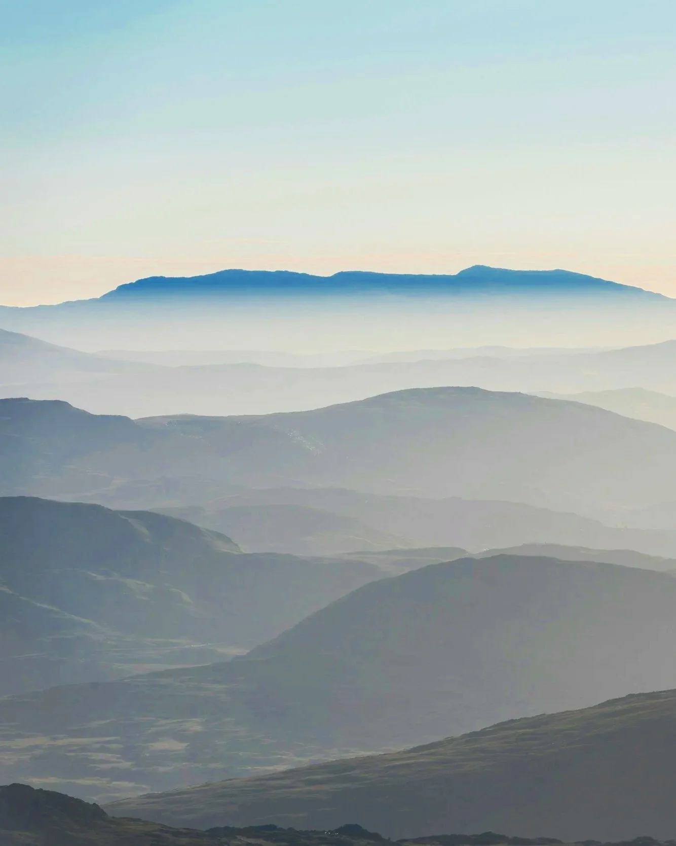 A landscape of layered mountains with mist or clouds, showing a range from dark foreground to lighter background, with a clear sky.