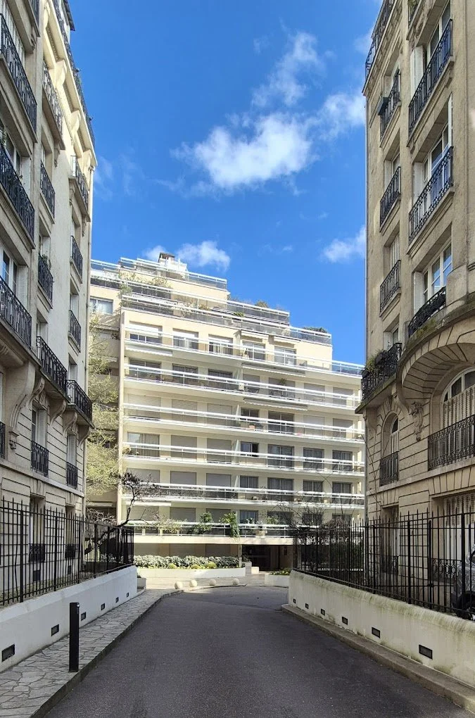 Vue d'une cour entre des immeubles résidentiels modernes avec un bâtiment blanc à plusieurs étages et un ciel bleu avec quelques nuages.