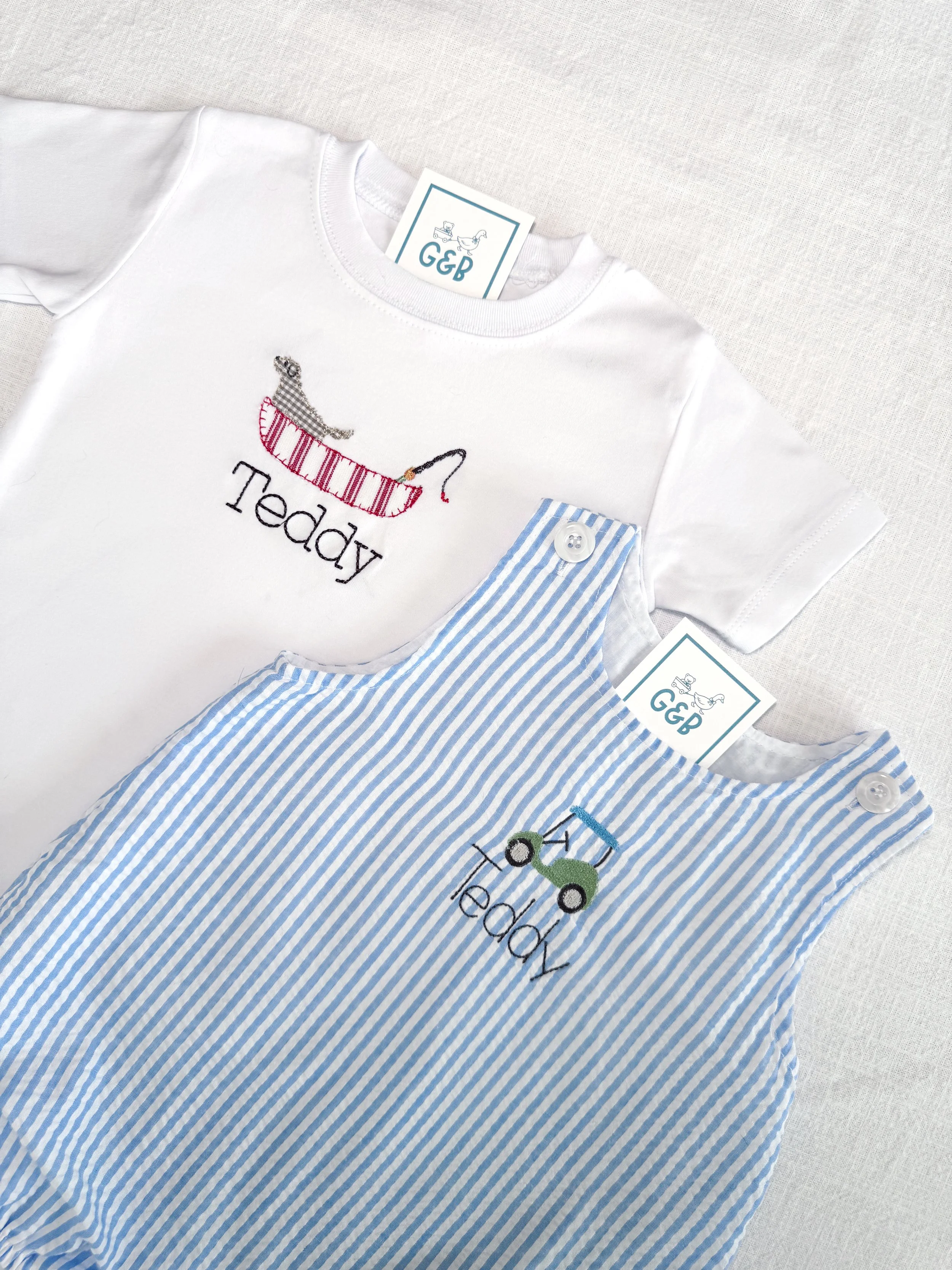 Two small children's shirts with embroidered designs and tags, lying on a light-colored surface.