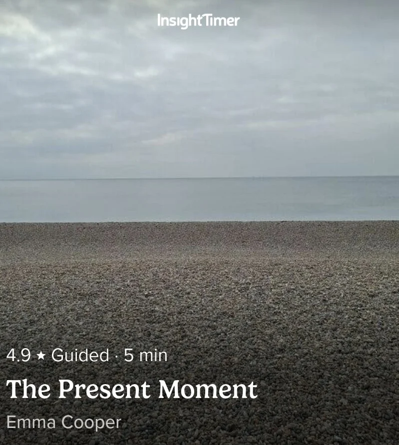 A calm beach scene with pebbles in the foreground, a body of water, and a cloudy sky, with an overlay of a guided meditation titled 'The Present Moment' by Emma Cooper.
