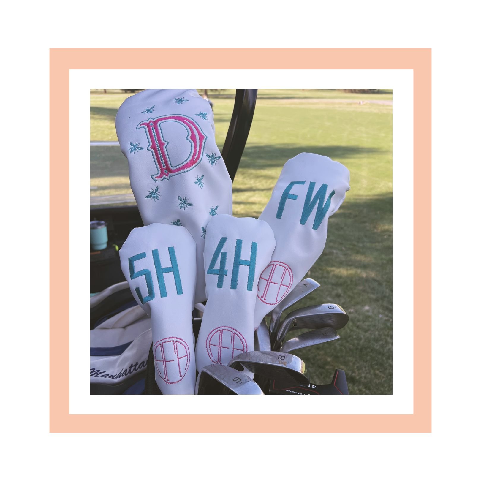 Golf club bag with white headcovers embroidered with pink and blue letters 'D', 'F', '4', '5', 'H', and a globe logo, set on a golf cart near a golf course.