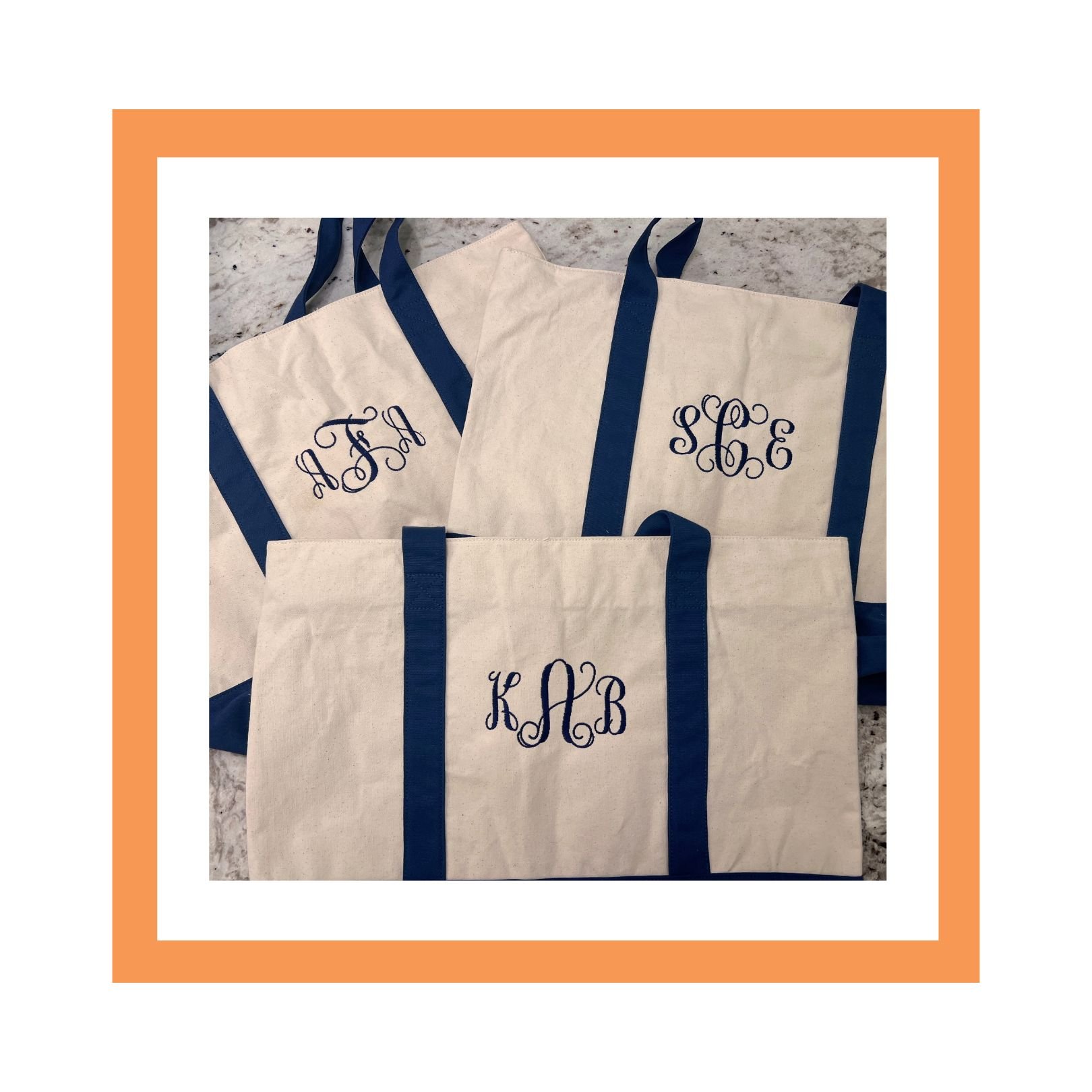 Several white canvas tote bags with blue handles and embroidered initials in block and cursive font, placed on a granite surface, framed by an orange and white square border.