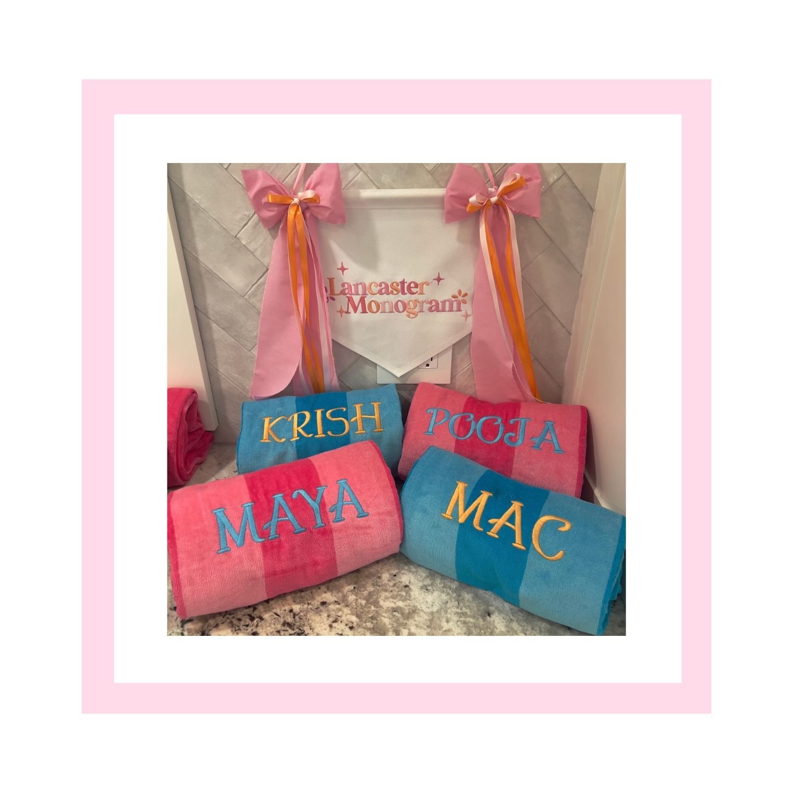 Display of monogrammed towels in pink and blue with names "Maya", "Macy", "Krish", "Poja", "Mac". Pink banner with bows and "Lancaster Monogram" in the background.