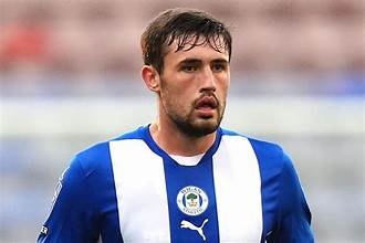 Soccer player with dark hair and a beard wearing a blue and white striped jersey on the field.