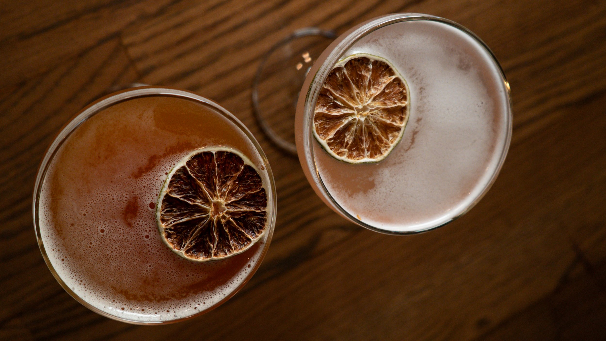 Two glasses of drink with dried orange slices garnish on a wooden table.