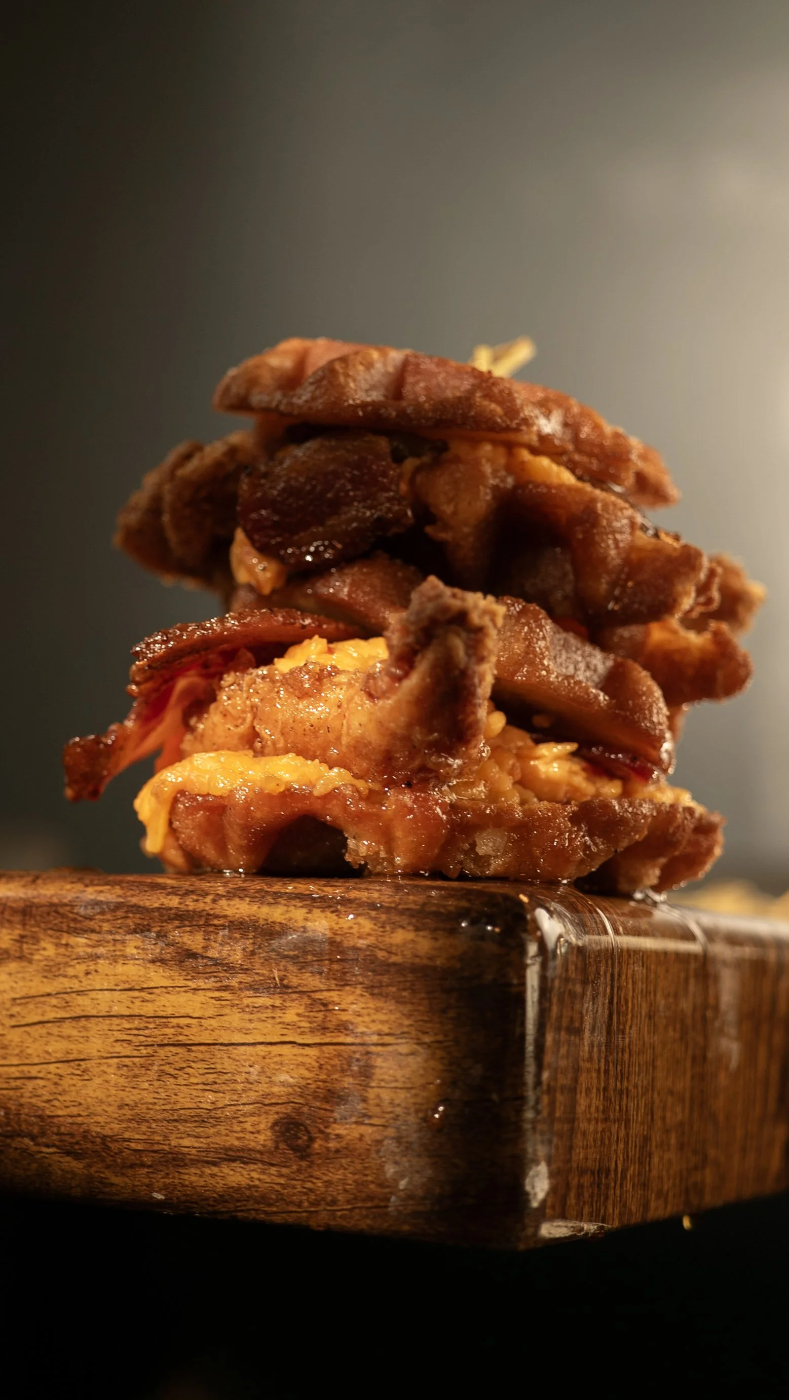 Stack of crispy bacon with melted cheese on a wooden board.