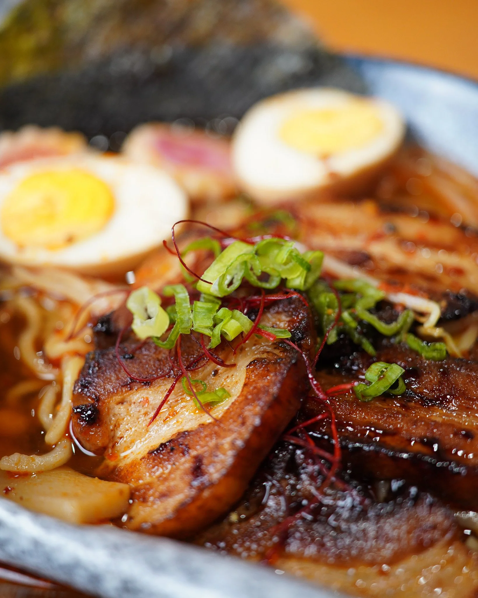 Close-up of a cooked dish featuring sliced hard-boiled eggs on top of a bed of noodles and sauce, garnished with chopped green onions and microgreens.