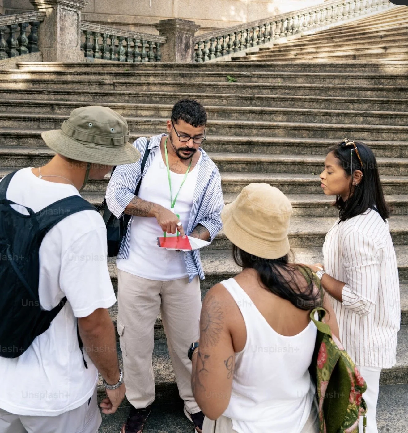 A group of five diverse individuals standing on an outdoor staircase, engaged in a conversation or discussion. One man is pointing at a device, possibly a phone or a small tablet, while others listen attentively.