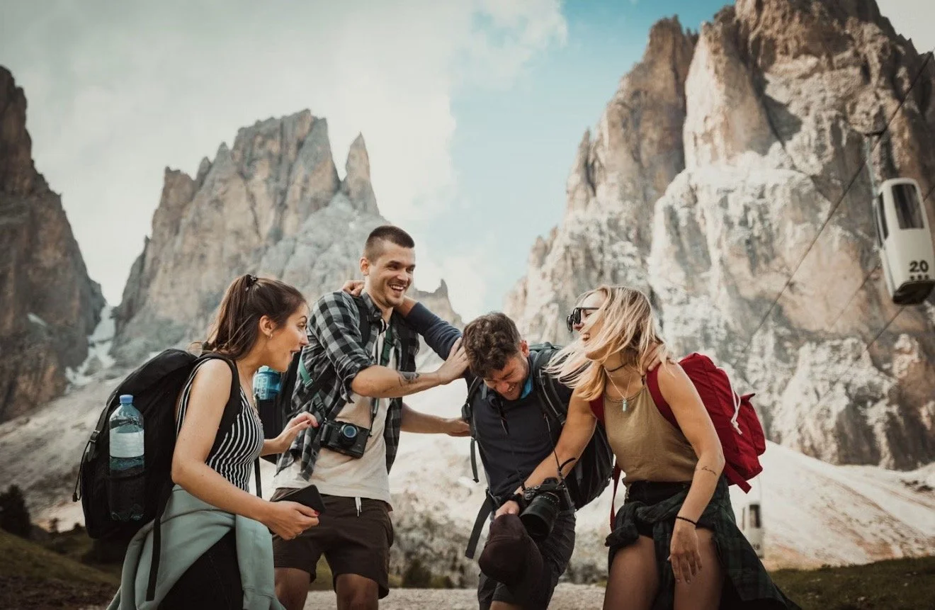 Group of four friends hiking in the mountains, smiling and laughing together, with rocky peaks in the background.