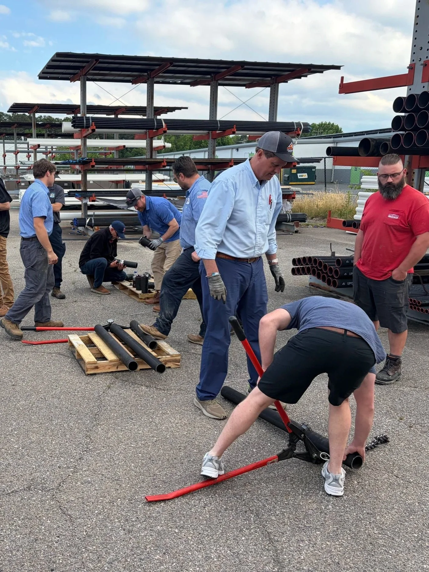 Group of workers assembling cast iron pipes outdoors, with shelving units and construction tools around them assembling a plumbing system with Charlotte Pipe and Foundry Cast Iron.