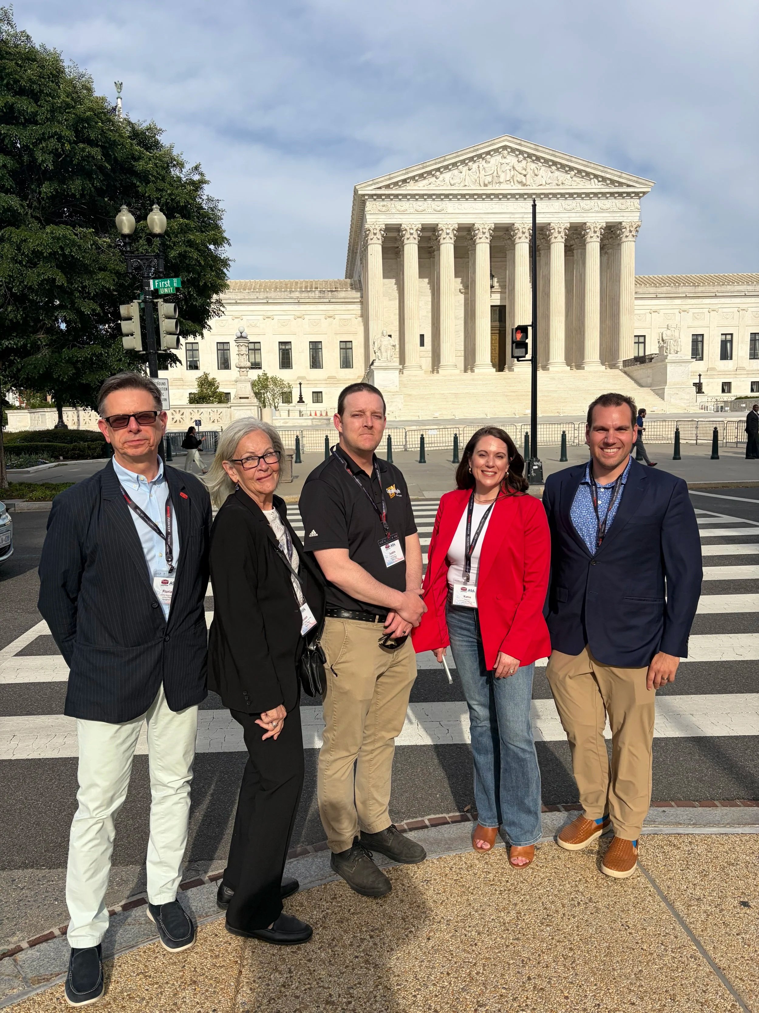 A group of five diverse people standing in front of the United States Supreme Court building in Washington, D.C., posing for a photo.