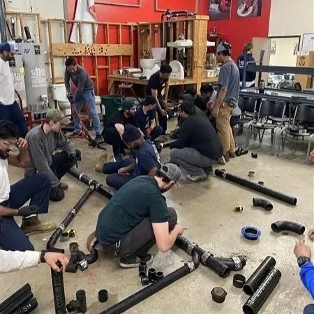 Group of students working on plumbing projects with pipes and fittings in a classroom or workshop setting.