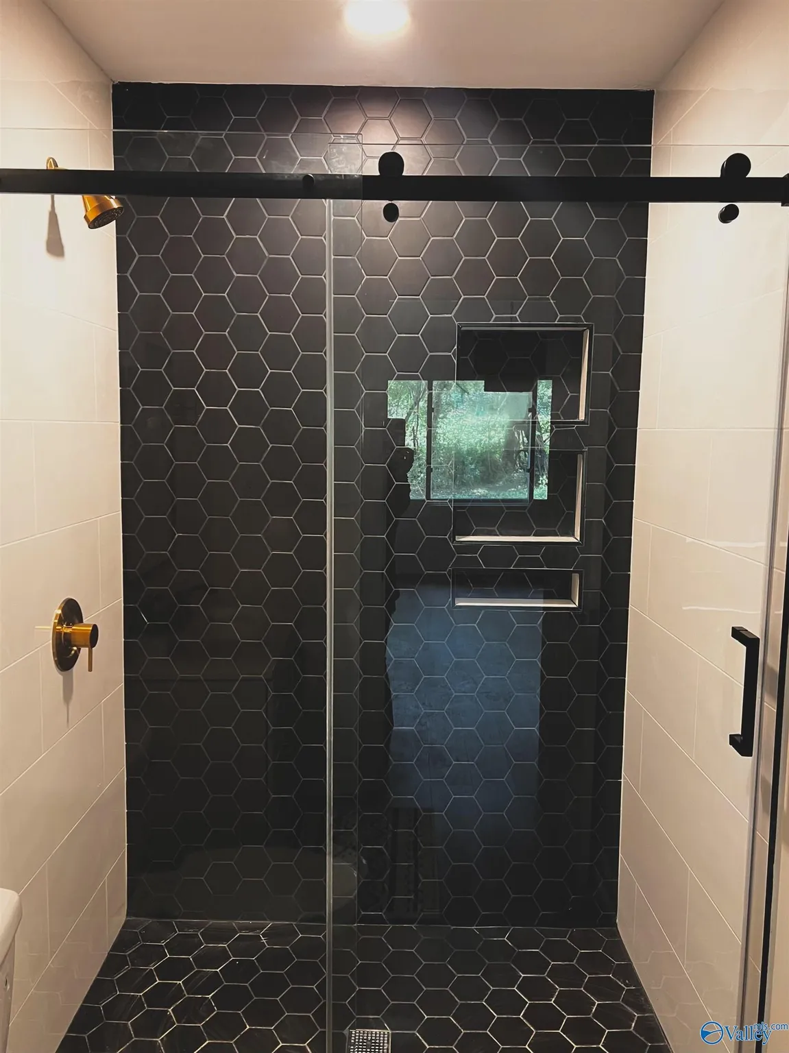 Black-tiled walk-in shower with hexagonal tile pattern, a window with multiple panes, and a glass door.