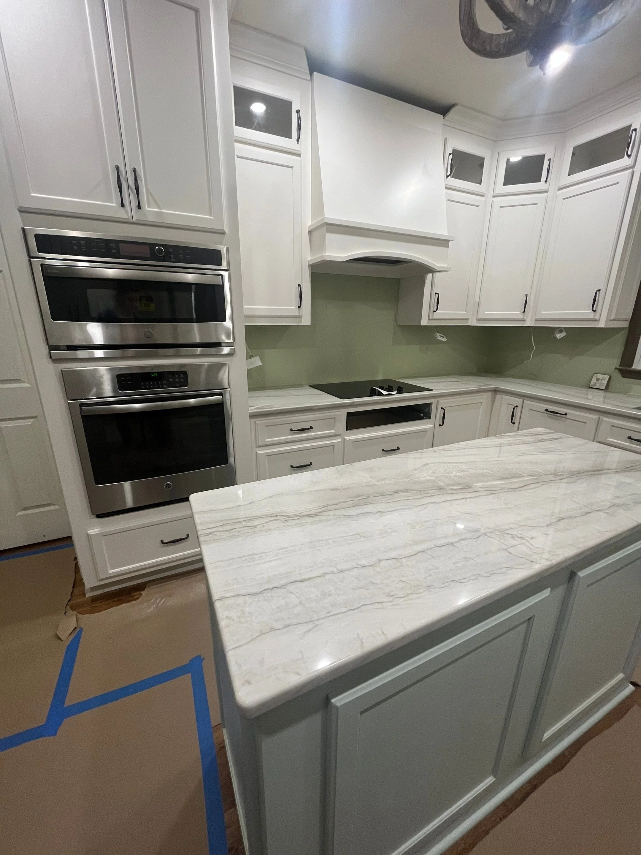 A kitchen with white cabinets, a marble countertop, and stainless steel appliances, including an oven and microwave. There is a green wall behind the counter and a note or picture on the countertop to the right.