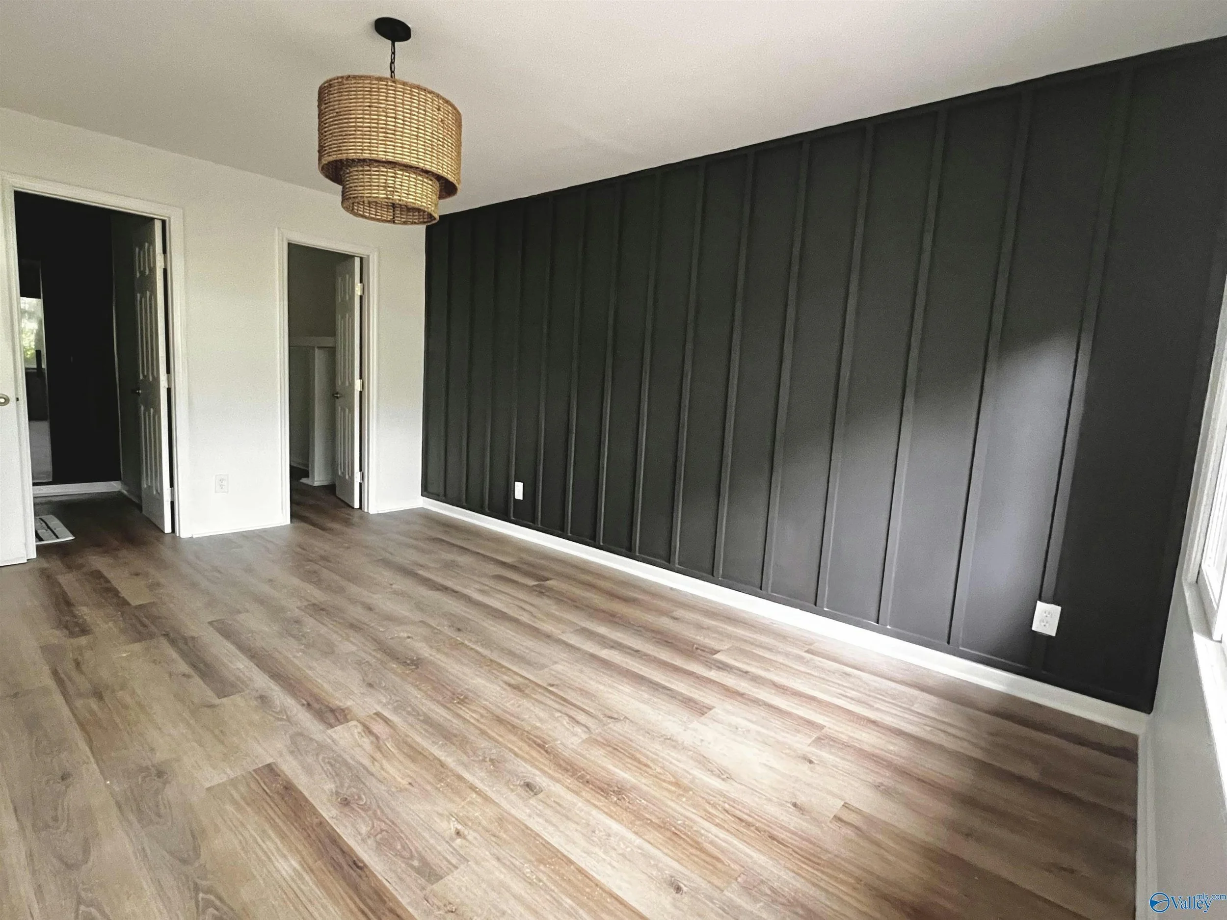 A room with a dark accent wall, light wood flooring, and a hanging wicker light fixture.